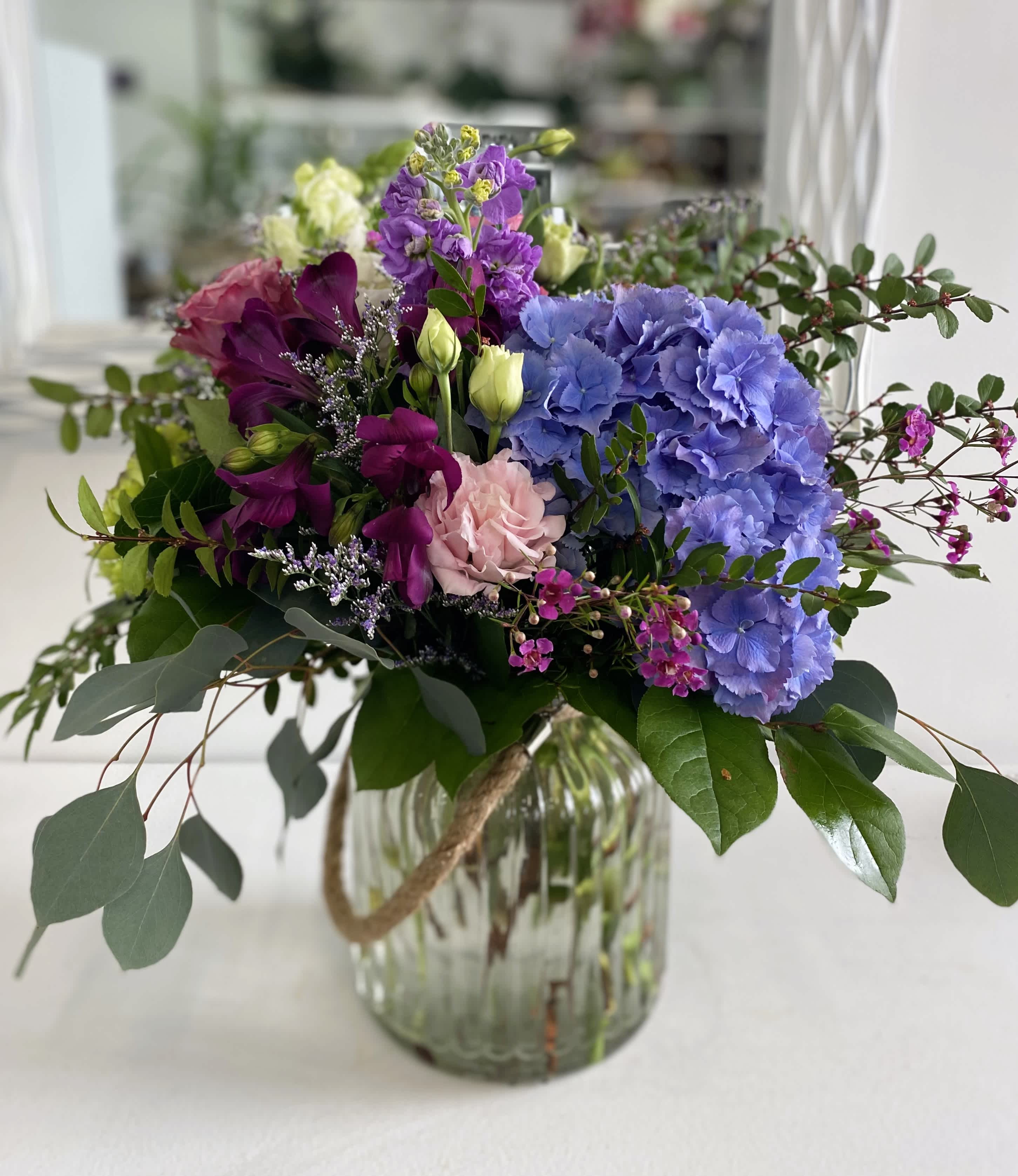 Moody Blooms Moody Blooms - A moody blend of blue, purple, and pink blooms arranged into a keepsake glass vase with lush mixed greenery and airy filler flower.