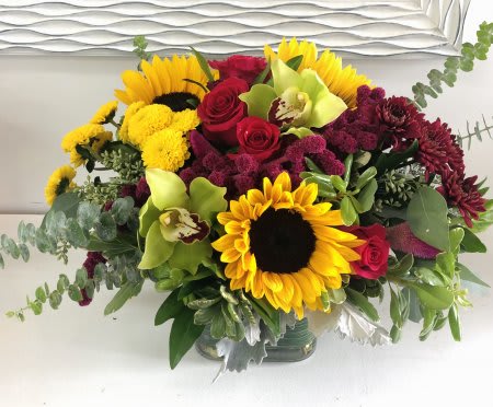 Vibrant Vase Design Vibrant Vase Design - Gorgeous sunflowers and roses arranged in a glass vase with warm-toned blooms and mixed greenery.