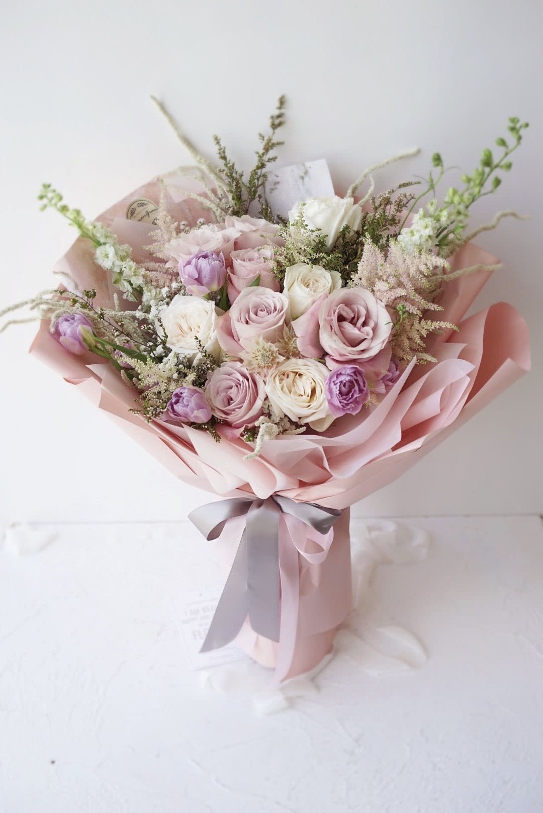 Blush bouquet A1 - Ethereal Blush Bouquet – A Timeless Expression of Elegance  Drift into a world of romance with this dreamy bouquet, featuring soft pink and ivory roses, delicate lavender tulips, and wisps of astilbe and wildflowers. Wrapped in a luxurious pastel pink paper and tied with a graceful satin ribbon, this arrangement is perfect for celebrating love, beauty, and heartfelt moments.   A delicate blend of elegance and charm  Perfect for weddings, anniversaries, or a thoughtful surprise  Handcrafted with fresh, premium flowers for lasting beauty  Create an unforgettable moment—order this enchanting bouquet today!