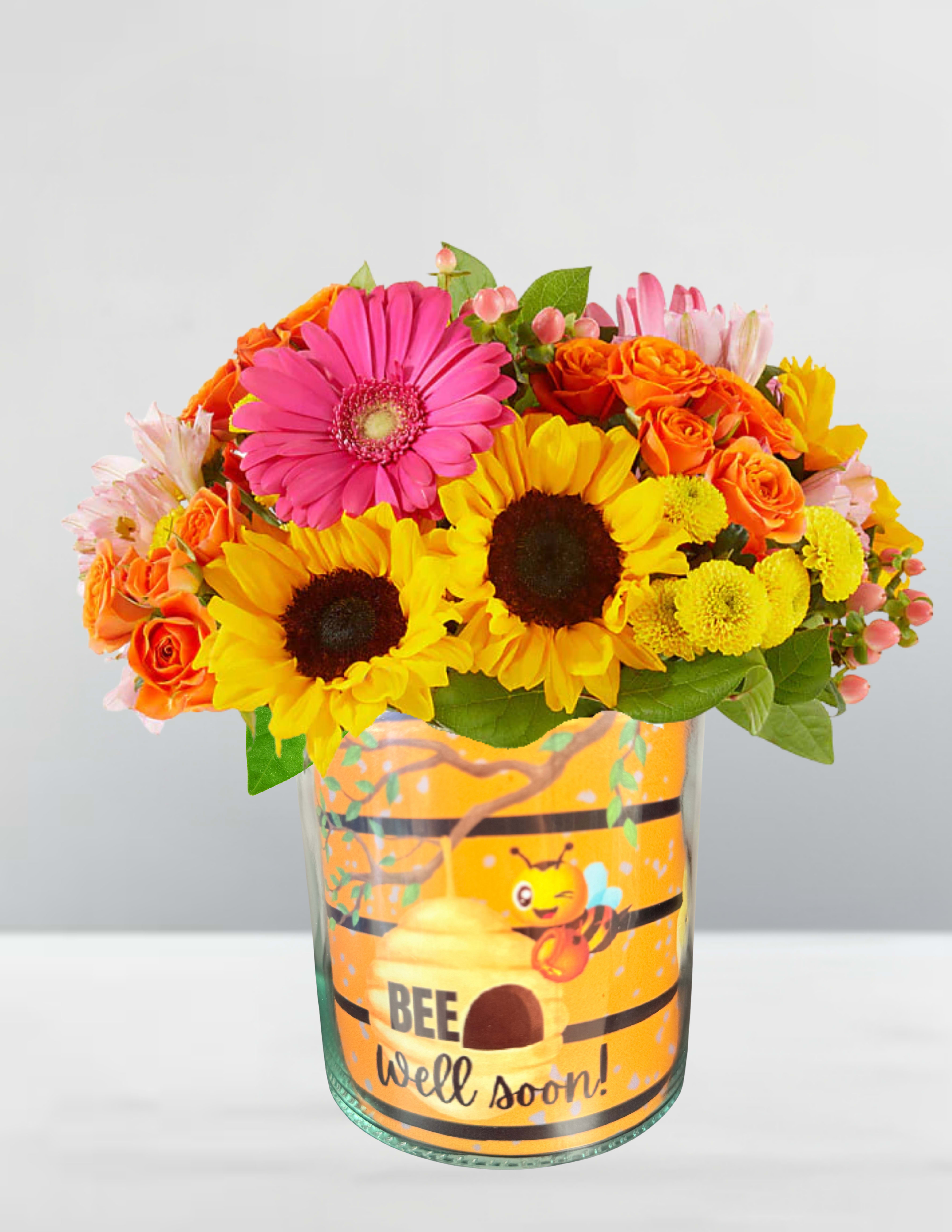 Bee well soon - Bee well soon Buzzing Back to Bloom Send a burst of sunshine and sweetness with Buzzing Back to Bloom, a vibrant get-well bouquet that hums with warmth and optimism. Nestled in a playful bee-themed vase, this arrangement features golden sunflowers, coral roses, pink gerbera daisies, and delicate alstroemerias—each bloom chosen to lift spirits and brighten days. The cheerful “BEE well soon!” message adds a touch of humor and heart, making this the perfect pick-me-up for someone on the mend. Like a garden kissed by morning light, it’s a gentle reminder that healing is a journey—and joy is part of the cure.