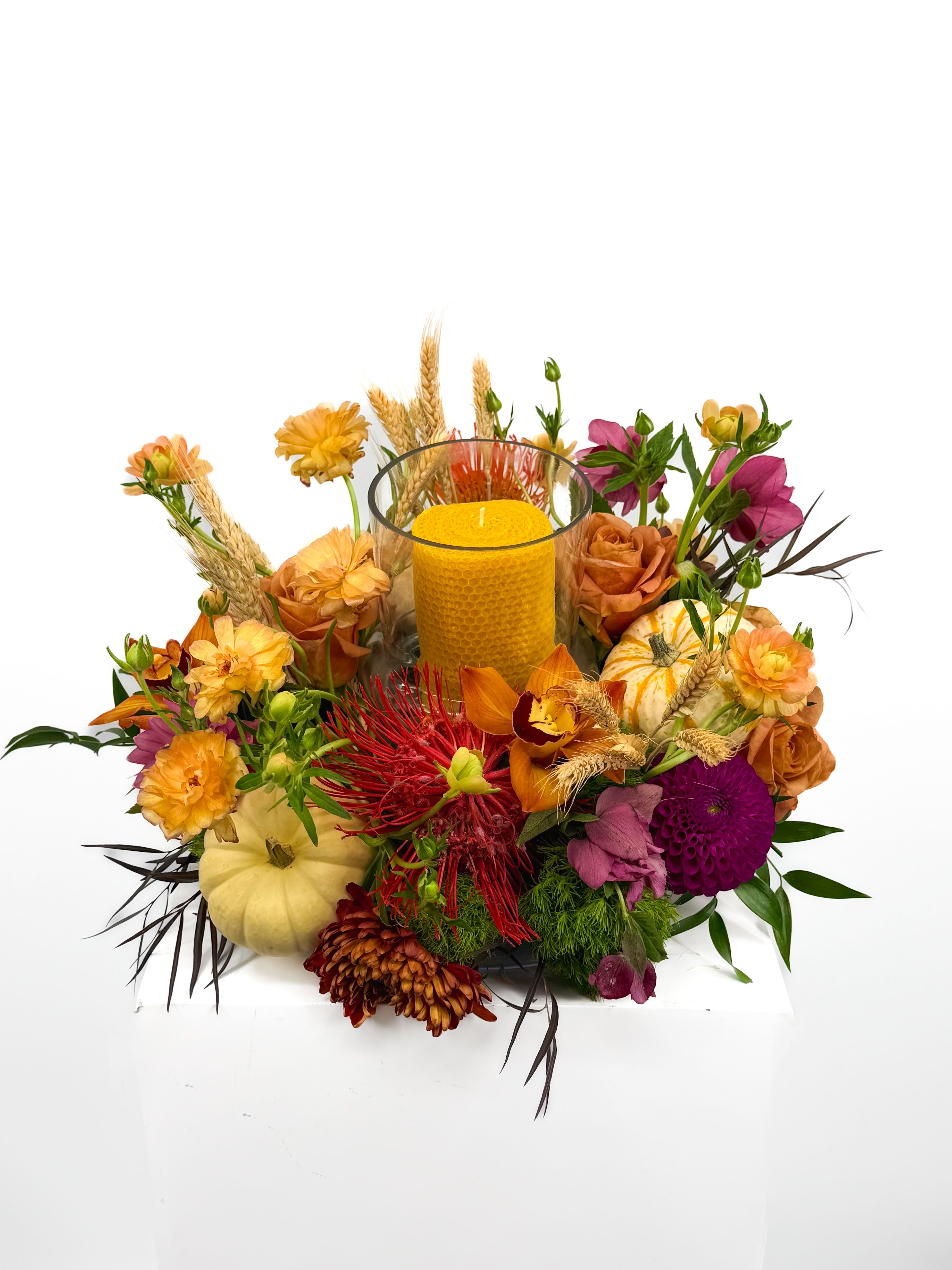 Nectar - Vibrant golden beeswax candle rests in a clear glass vase, surrounded by a lush mix of seasonal blooms in warm tones of orange, crimson, and plum. Accented with mini pumpkins, wheat stalks, and fresh greenery, this handcrafted design adds a perfect touch of rustic sophistication to any occasion.  -Ideal for: • Thanksgiving gatherings • Autumn weddings • Seasonal home décor • Gift giving