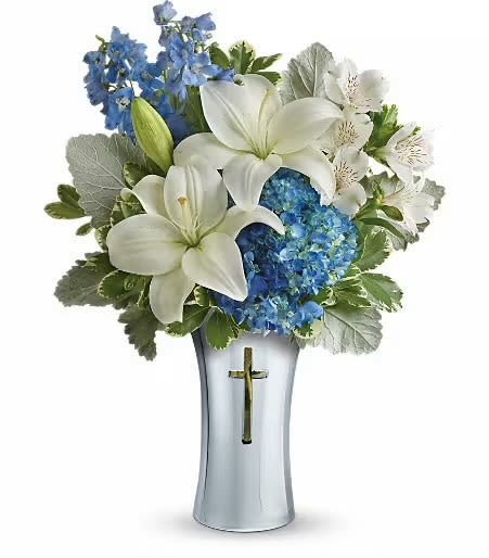 Divine Grace  - This graceful and serene bouquet is beautifully composed in a silver-toned vase featuring a subtle, elegant cross inset on the front—making it a perfect tribute piece for the Easter season or a spiritual celebration.  The arrangement itself is a refreshing mix of soft whites and soothing blues, with a peaceful, uplifting tone. Creamy white lilies are the focal point, their large, open blooms exuding elegance and purity. They’re complemented by delicate white alstroemeria, adding a light, airy feel. Surrounding them are lush clusters of blue hydrangea and tall blue delphinium, creating a rich contrast and giving height and fullness to the display.  The overall effect is peaceful, spiritual, and refined, making it ideal for Easter services, memorials, or a centerpiece that quietly celebrates hope and renewal.