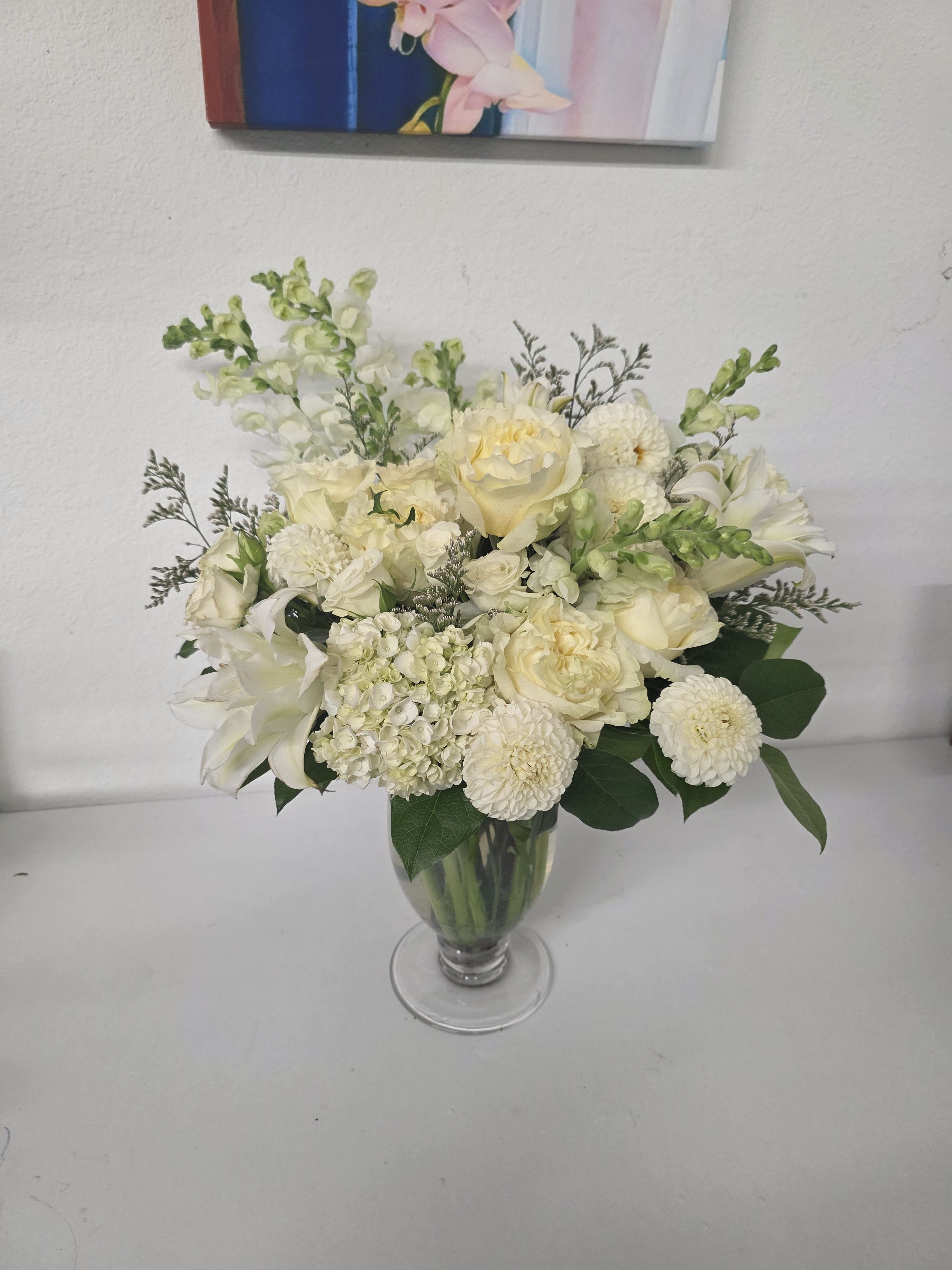 Whispering White - A beautiful arrangement of white garden roses, lilies, snap dragons and other beautiful filler. This gorgeous piece is sure to make a statement and to bring joy to the one you care for. 