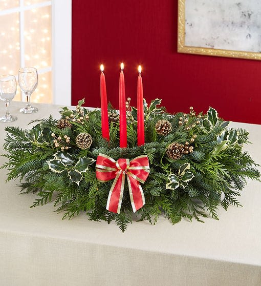 Grand Holiday Greenery Centerpiece (Greens Only - No Flowers) Grand Holiday Greenery Centerpiece (Greens Only - No Flowers) - Isn't it grand when family and friends gather around the holiday table? Equally grand is our classic holiday centerpiece. A generous gathering of fresh evergreens, adorned with pinecones, berry clusters, holly leaves, and a vibrant bow. This centerpiece features three elegant tapered candles in the center to cast a warm glow over every festive celebration.