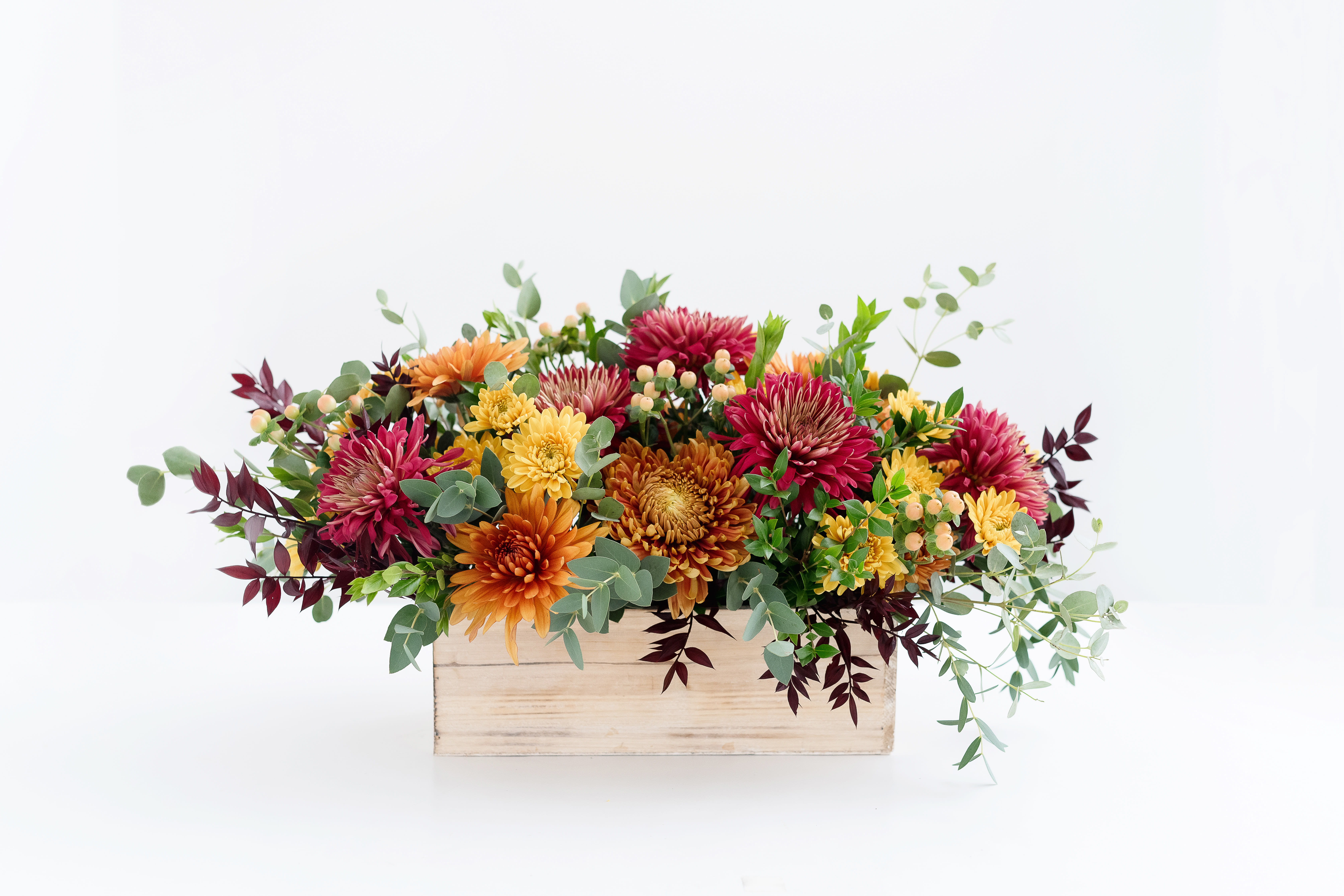 Autumn Cottage - Medium Box Arrangement - The best of fall! A stunning combination of premium, fall-colored mums paired with peach Hypericum berries, eucalyptus, and red Italian ruscus, all beautifully arranged in a white-washed wooden box. Perfect for your Thanksgiving table or as a thoughtful gift for someone special.  Measures approximately 7&quot; tall x 15&quot; long.