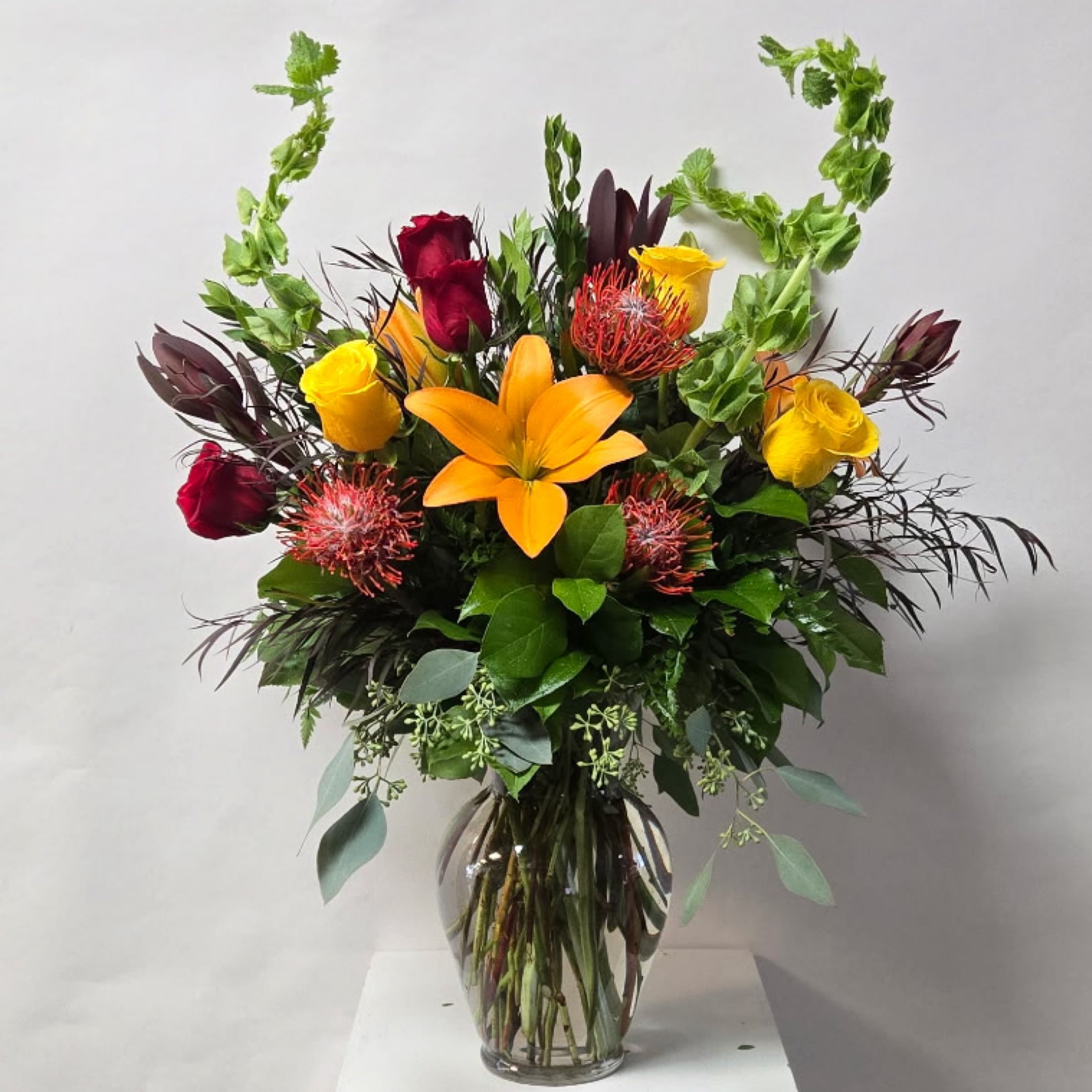 Fall and Vibrant Fall and Vibrant - This Tall Arrangement Includes Orange Lilies, Red Roses, Yellow Roses, Safari Sunsets and Pincushions. Or as Similar as Possible.