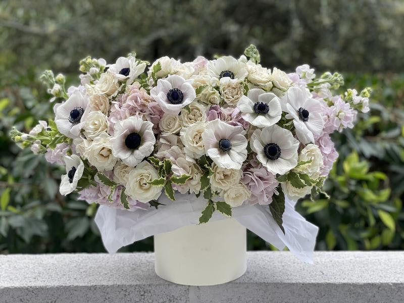 Rose &amp; Hydrangea Mix - This exquisite pink flower box is an exclusive design from your premier Los Angeles florist. This arrangement is a romantic masterpiece combining soft textures and contrasting colors.  It features stunning, velvety pale pink hydrangeas as the base, complemented by fragrant garden roses in cream and blush tones. The arrangement is crowned with gorgeous white anemones, whose deep black centers provide a striking, modern focal point. This signature anemone rose arrangement is perfect for those seeking luxury and sophistication.  Ideal for special occasions like anniversaries, birthdays, or high-end congratulations. We guarantee the highest quality and the freshest blooms for every order, ensuring an unforgettable gift.  Take advantage of our professional and reliable LA flower delivery service across Greater Los Angeles. Order this magnificent centerpiece today for swift fresh flowers LA delivery!