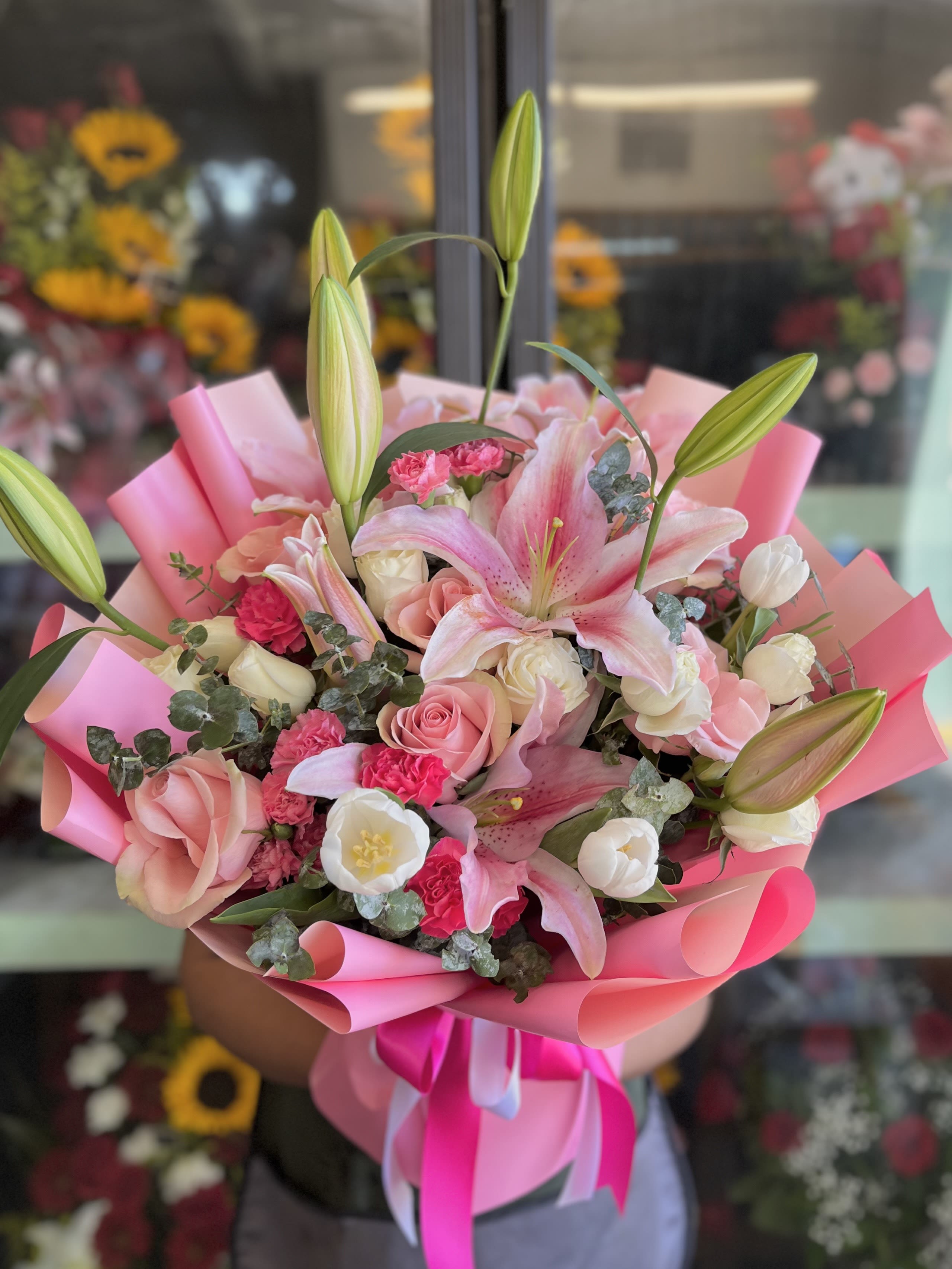 Tulip Blossom Korean-Style Bouquet - Inspired by refined Korean floral design, this elegant bouquet features a graceful mix of tulips, pink oriental lilies, white and pink toned roses, and hot pink mini carnations, all thoughtfully arranged with touches of fresh eucalyptus for added texture and movement.  Wrapped in delicate blush toned Korean wrapping paper, this bouquet blends soft femininity with modern minimalism, making it a perfect choice for birthdays, celebrations, or simply expressing love in a subtle, stylish way.