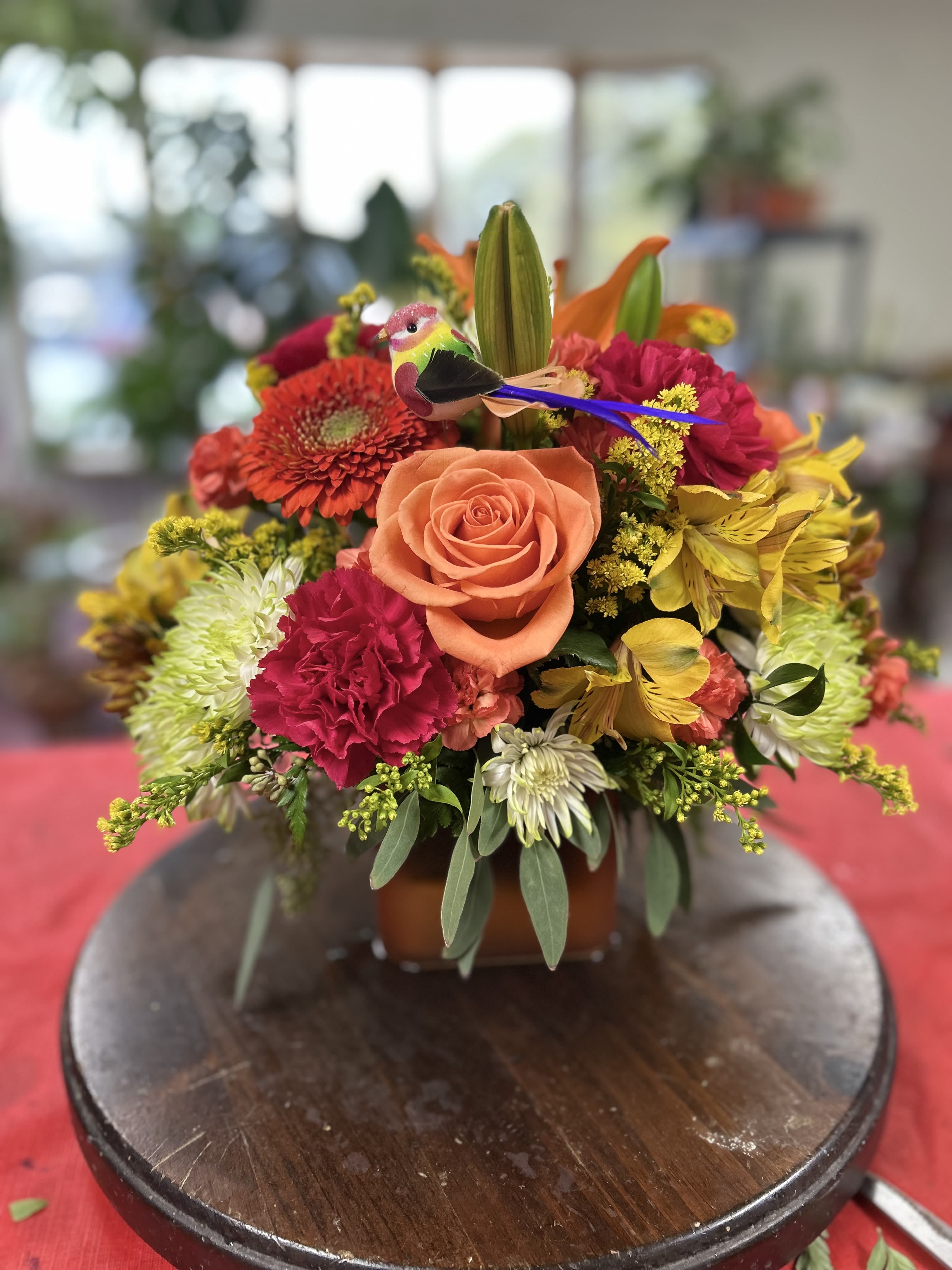 Bright Sunset - This charming vase overflows with a vibrant seasonal mix of roses, marigold, chrysanthemums, all complemented with fall foliage and accents, carefully designed in a classic glass cylinder vase. The harmonious blend of oranges, yellows, purples and reds, provides a beautiful array of color and textures that can uplift every room.  Depending on availability, substitutions of specific flowers may be necessary, however, the overall look will be as similar as possible.