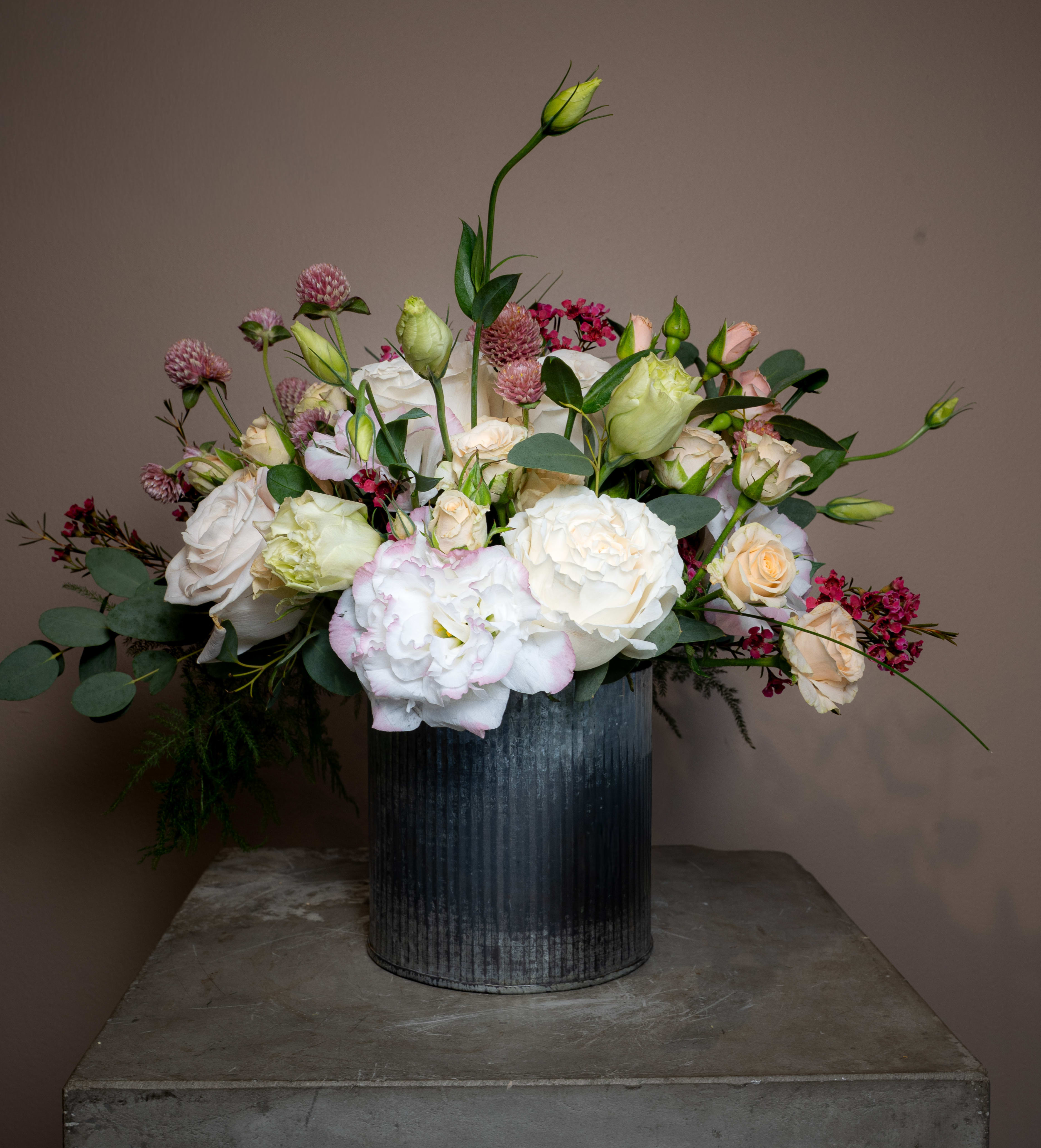 Sulla Varanda - Beautiful white roses, lisianthus, clover, and more, juxtaposed by this galvanized metal vase, create a beautiful piece perfect for any occasion.