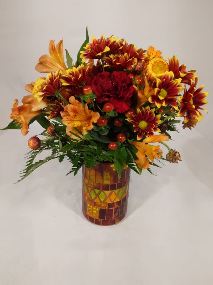 Sunset Glow - This beautiful Fall arrangement has Burgundy Carns, Orange Alstro, Red Hypericum Berries, Bronze Strawflower and two-toned daisies in a beautiful mosaic vase.