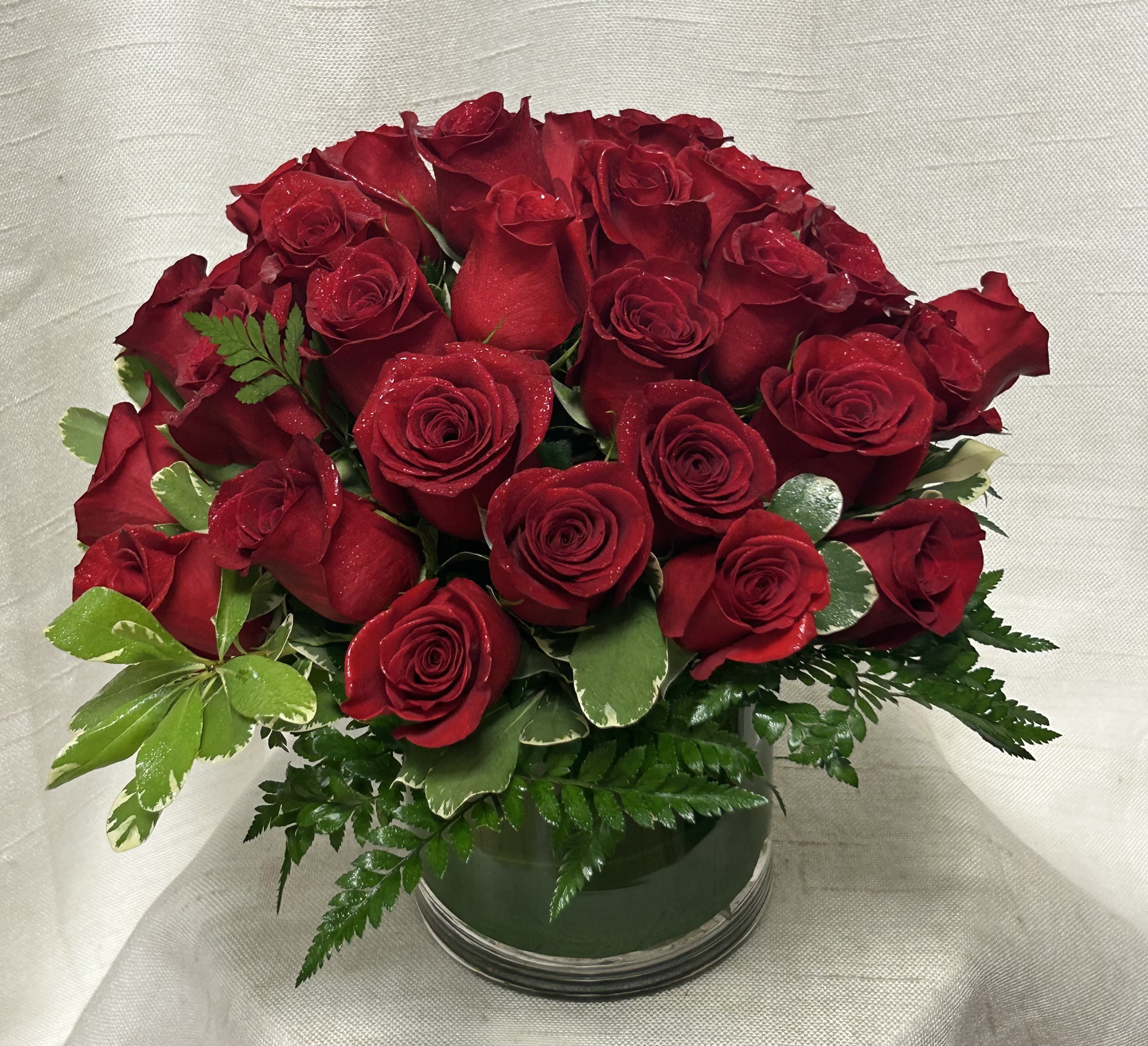 Passionate (DL) - Ignite passion and romance with our exquisite arrangement of 24 red roses, artfully arranged in a sophisticated cylinder vase. This stunning display is designed to convey love and desire. Each rose is handpicked for its velvety petals and deep crimson hue, symbolizing true love and passion.