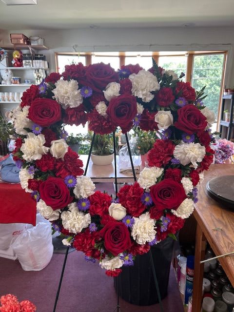 An American Tribute I - A Tender Tribute: The red Elegance Wreath In times of reflection and remembrance, a tender tribute embodies the love and memories shared with a precious loved one. he red  Elegance Wreath is a beautiful and heartfelt expression, meticulously crafted to convey both grace and serenity.  Mounted on a sturdy easel, this wreath measures approximately 24 inches in diameter, making it an elegant and dignified tribute. Its circular shape is a poignant reminder of the unending circle of love and life.