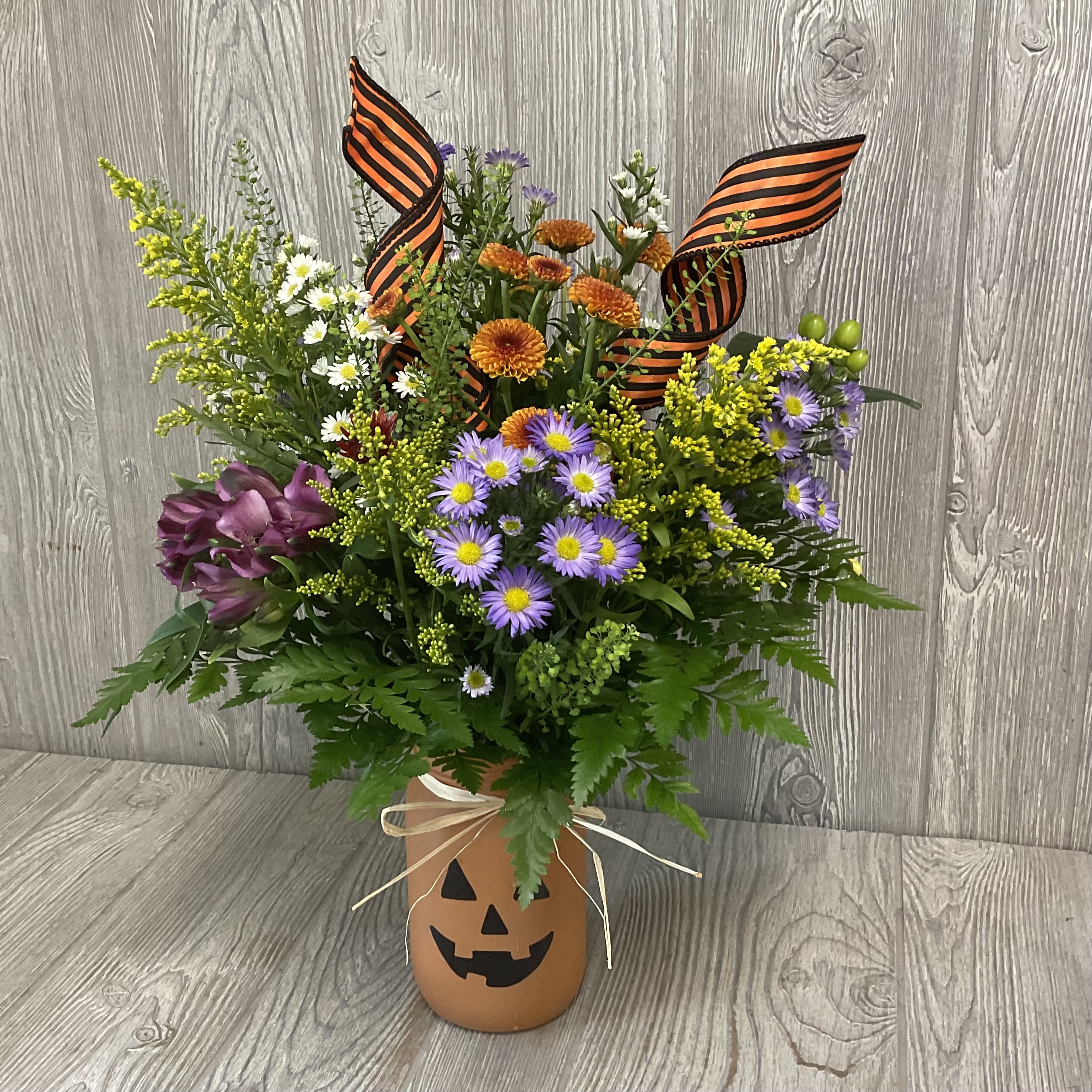 Jack-o’-Lantern Wildflower - Arranged in a keepsake Jack-o’-Lantern glass jar with spooky Halloween inclusions. Unique wildflower arrangement designed to look like the flowers were fresh picked along the way. Each one is uniquely made making it to where no two are alike.