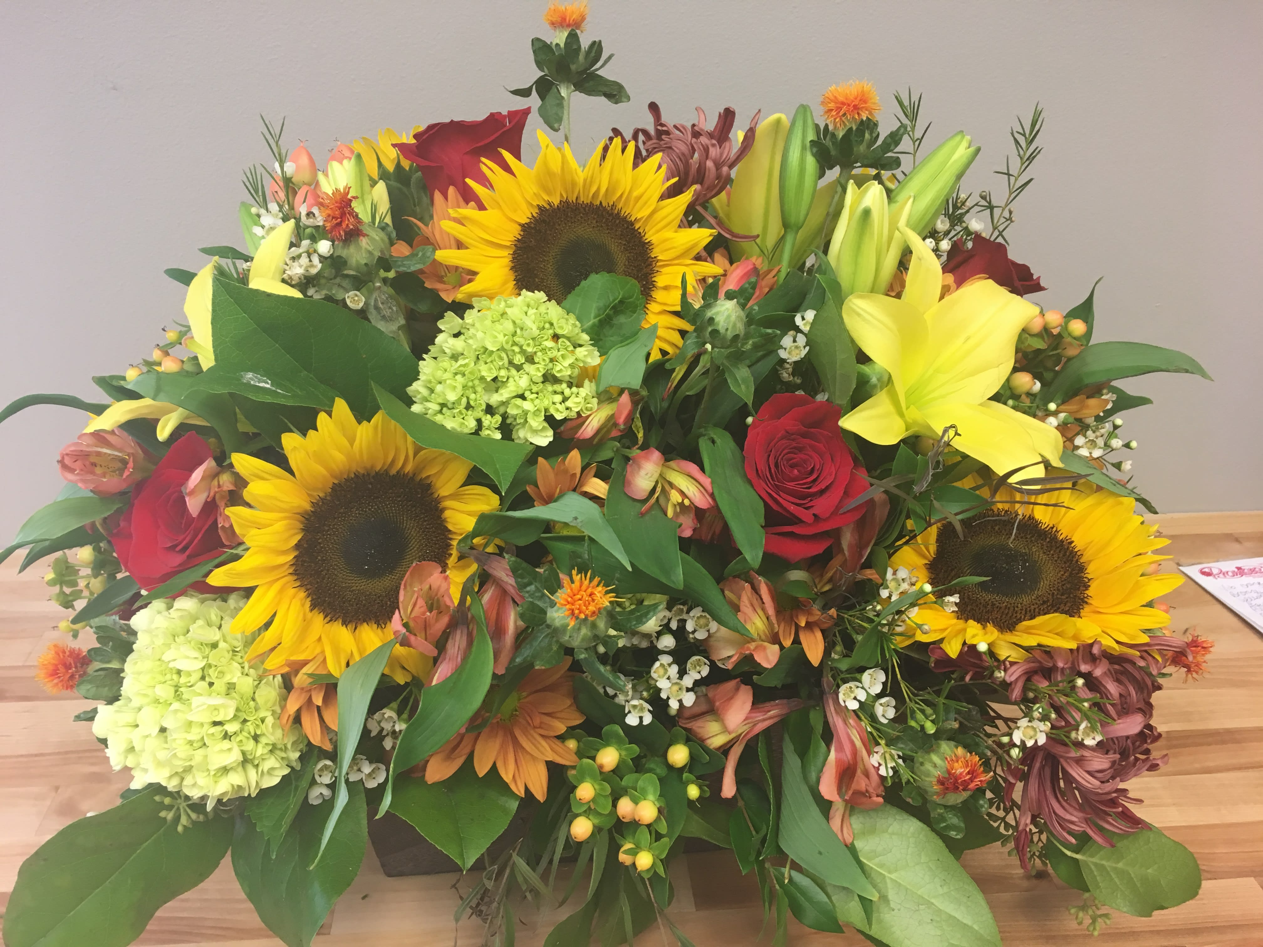 Sun powered -  Bright and boldl colors featuring sunflowers in this large floral arrangement.  Designed in a modern wooden cube- loaded full of the colors and flowers of the season.    We custom create each piece- based on availability and seasonality of flowers, and want each arrangement to be one of a kind.  Be assured- your arrangement will have the look and feel you've chosen.  Please feel free to leave comments for the designer you would like us to take into account in designing your unique arrangement.  If you prefer a different color combo (holiday, pastels, white, for example, please designate that in the florist instructions section on your order.  This arrangement requires at least 24 hours notice.