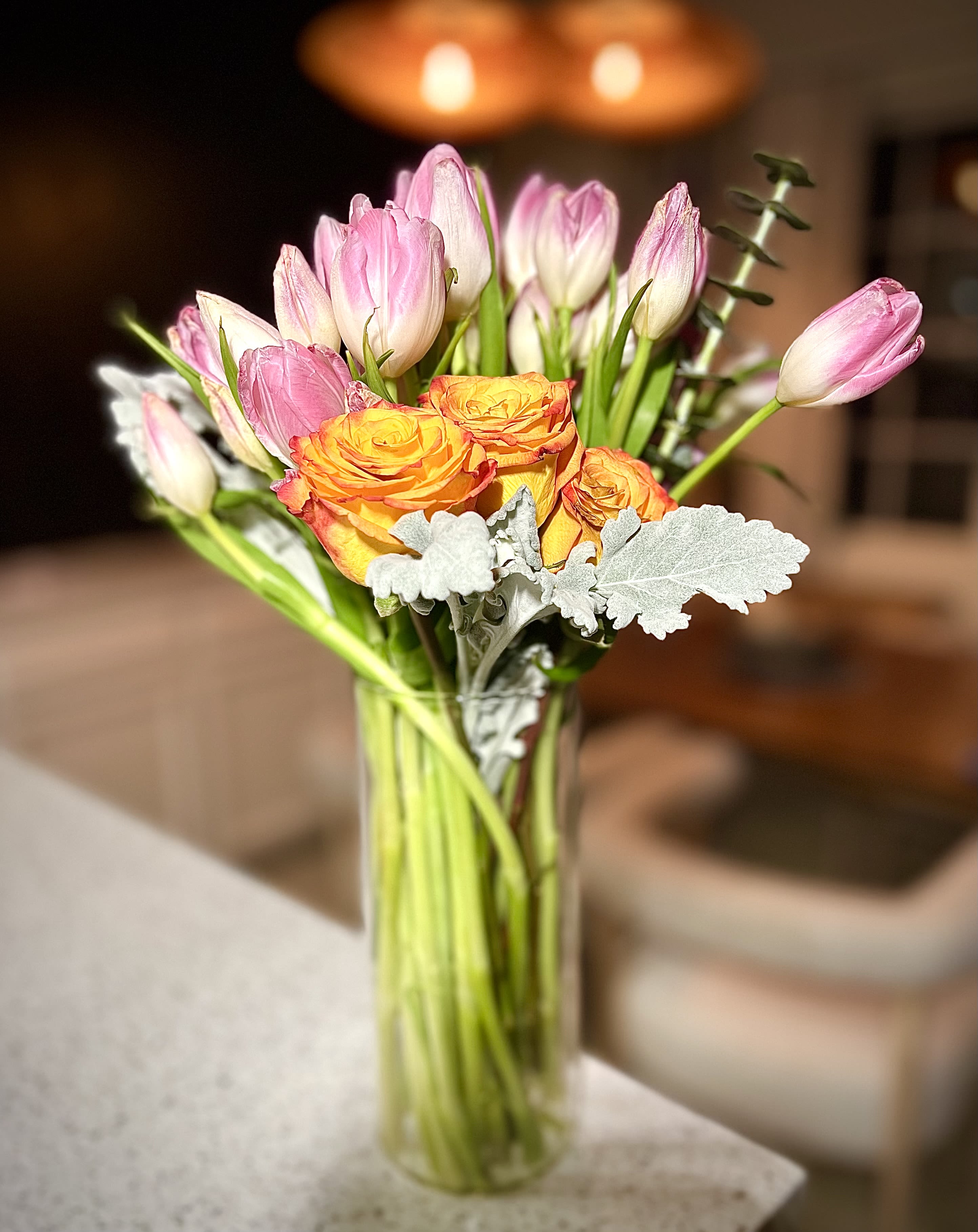 Sunset Elegance -  Elegant Tulip &amp; Rose Bouquet for Sale!   Bring warmth and elegance to your space with this stunning floral arrangement! Featuring delicate pink tulips and vibrant orange roses, complemented by soft silver foliage, this bouquet is perfect for any occasion—whether it’s a gift, home decor, or a romantic gesture.   Fresh &amp; long-lasting  Arranged with love  Comes in a stylish glass vase