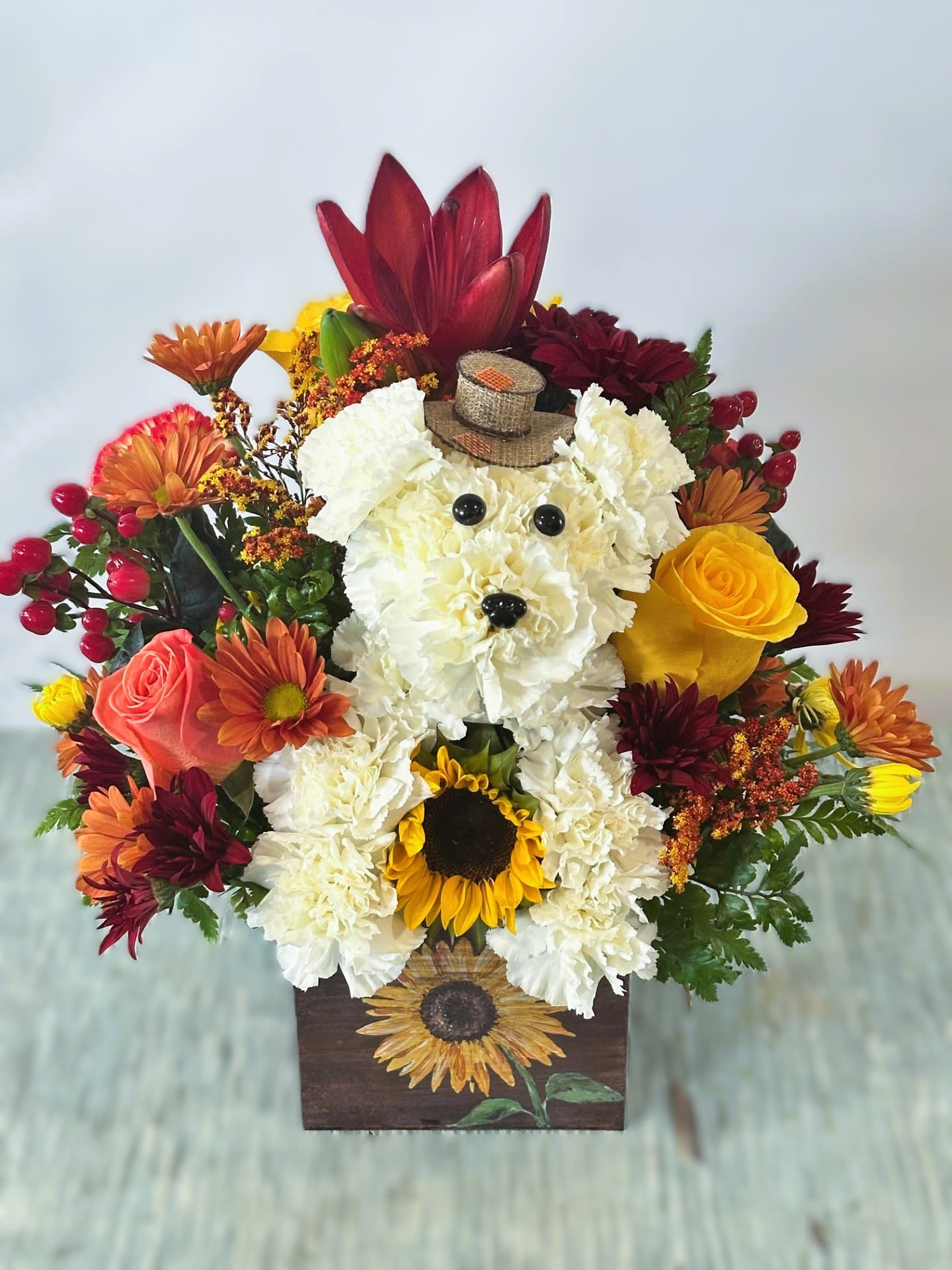 Autumn #4 - Fall color arrangement that includes a puppy with a hat made with white carnations. Arrangement created in a wood square planter with a sunflower design on the front that looks hand painted. Colors can be modified depending on availability. SAME DAY DELIVERY Please keep in mind we will try our best to make arrangement as similar as possible based on availability if a flower must be substituted we will keep arrangement within the same color scheme. 