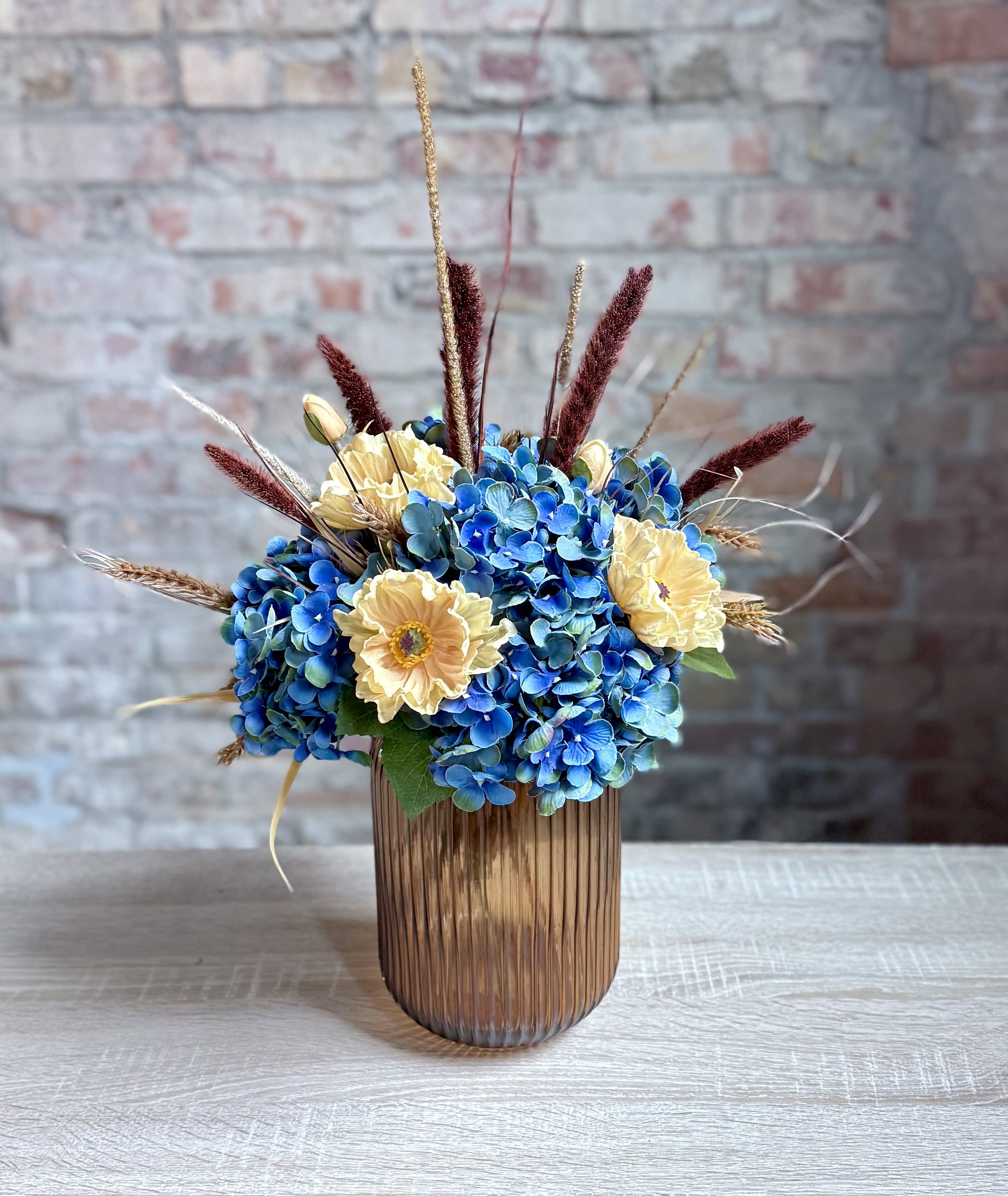 Faux blue and tan arrangement Faux blue and tan arrangement - A fun brown glass vase filled with all artificial flowers, hydrangeas, anemones and wild grasses.