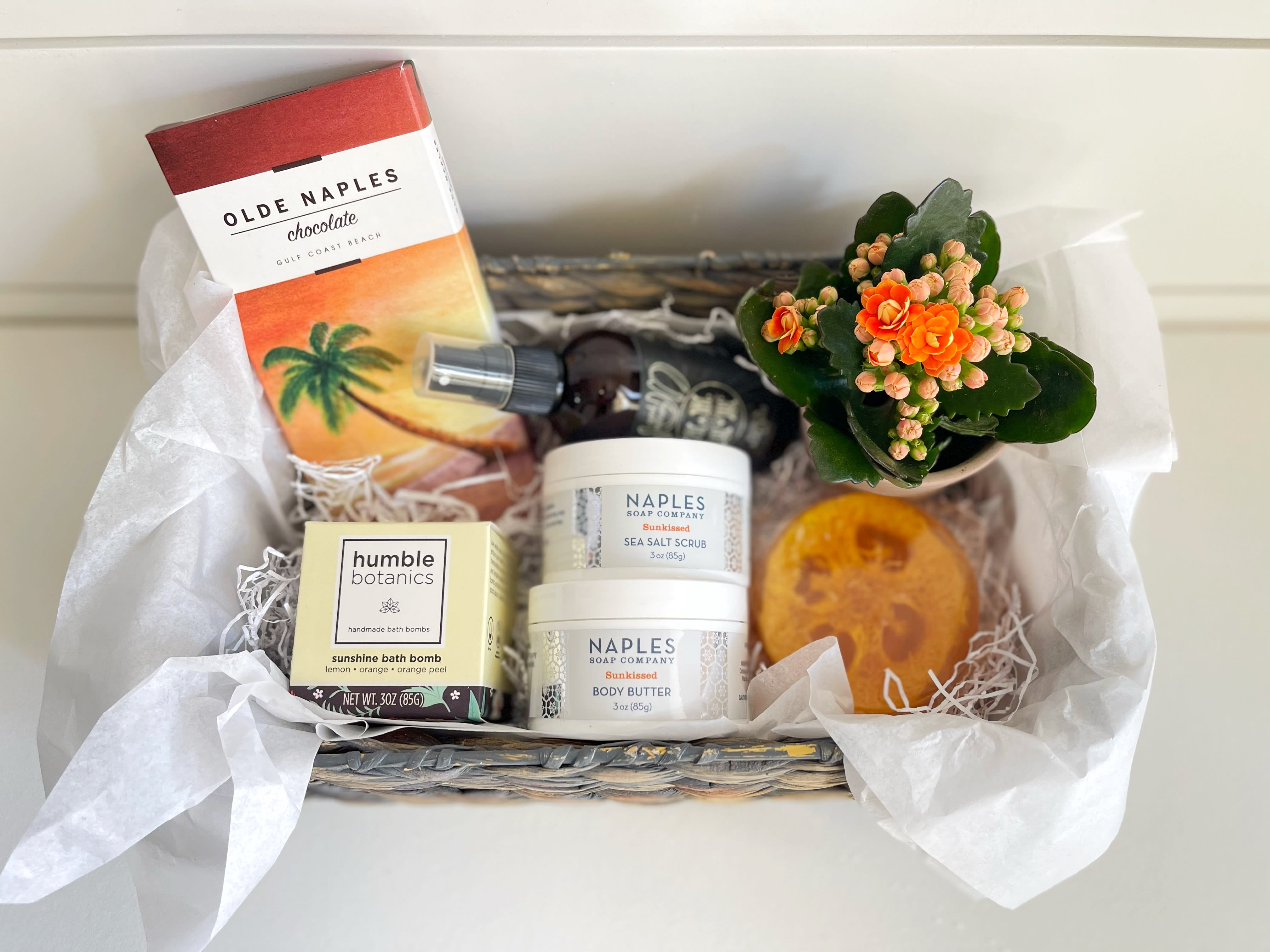 Tropical Bliss Gift Basket  - A pampering gift basket full of amazing tropical  themed products.  - Naples Soap Co. coconut water loofah soap - Naples Soap Co. Sunkissed body butter - Naples Soap Co. Sunkissed sea salt scrub -Humble Botanics Sunshine Bath Bomb. Instead of using harmful chemicals, dyes, and fragrances to achieve color and scent, Humble Organics has a non-toxic approach. They used dried orange peel, and organic orange and lemon essential oils. - Good Morning Sun room and body spray by Humble Love. A blend of mint and citrus specifically designed to help wake you up and keep you motivated.  - organic dark chocolate bar with sea salt from Olde Naples Chocolates. Box cover is original art work of Naples Beach. (can switch to milk chocolate if you add to the special instructions when ordering) - small potted plant with bright flowers. - quality reusable basket 