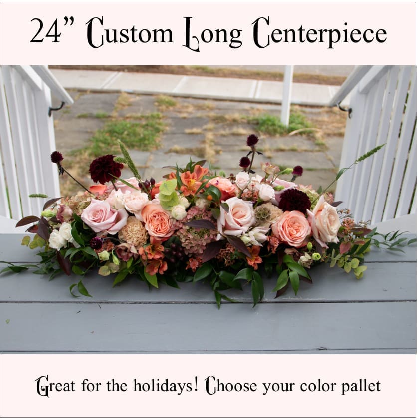 24" Custom Centerpiece 24" Custom Centerpiece - MINIMUM 24 HOURS NOTICE! The perfect centerpiece for your table at family gatherings and the holidays this is a 24" long arrangement with a low profile that appears as though the flowers are directly on the table. Les us know what colors you would like. Photo shows a DELUX arrangement which features more variety of textures and luxury blooms. If no color is given in the notes we will assume seasonal color pallet.