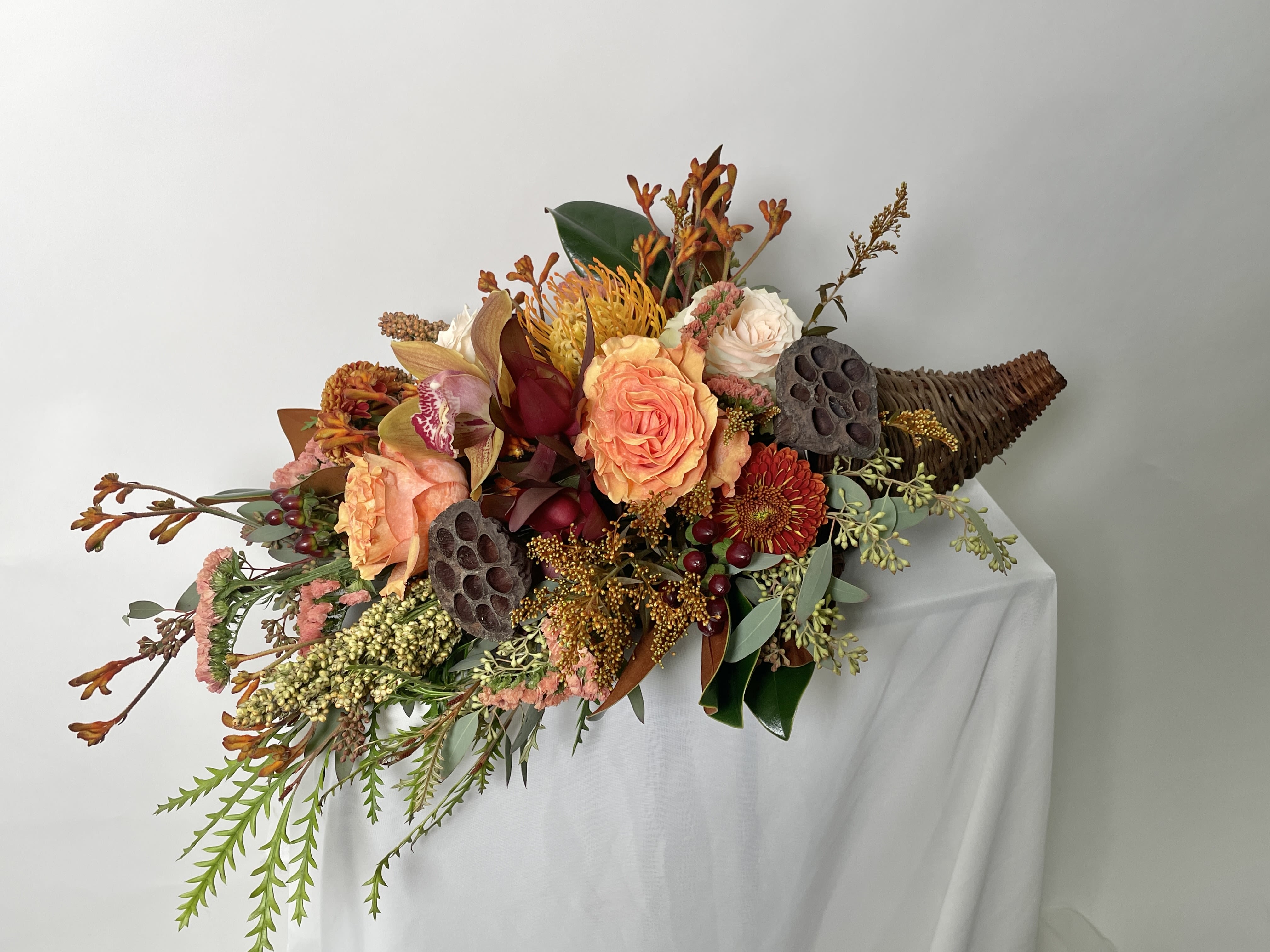 Cornucopia - A dark wicker cornucopia featuring a cascade of fall blooms and texture. A wide variety of textures, greens and seasonal flowers really give this design the feeling of lush harvest bounty. Perfect for the fall season or your Thanksgiving table. 