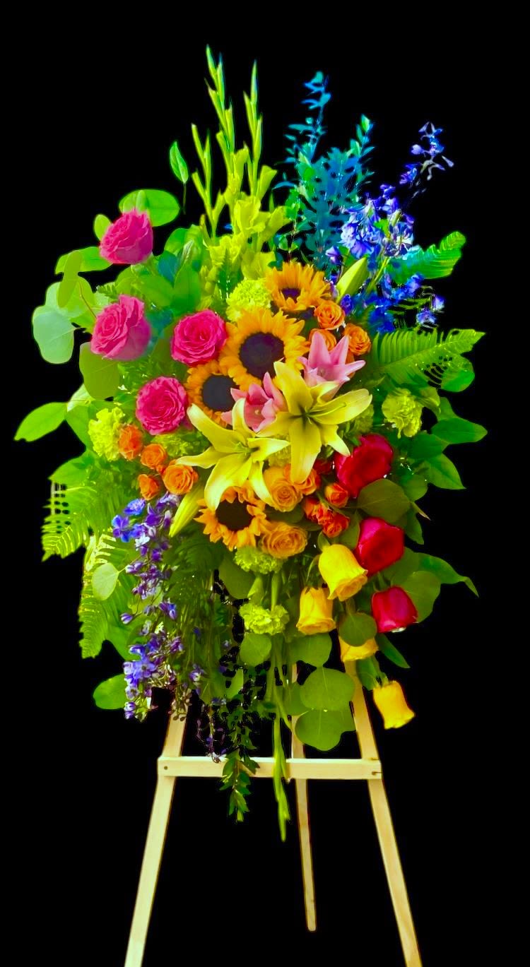 Vibrant Life standing spray  - This beautiful bright tribute includes blooms of every color of the rainbow. This design uses Sunflowers, Delphinium, Hot Pink Roses, Orange Roses, Green Gladiola, Green Carnations, Yellow Roses, and Pink &amp; Yellow Lilies and accented with various foliage. This design measures approx. 26&quot;W x 52&quot;H. 