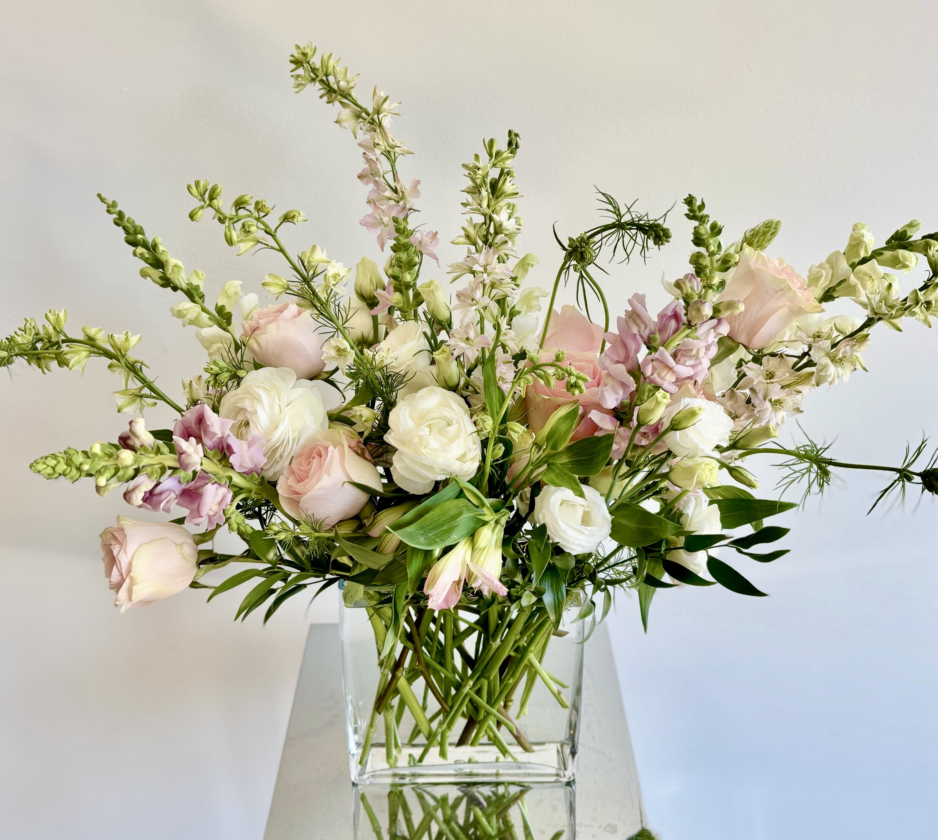 Isn't She Lovely - A lovely spring flower arrangement in soft pinks and whites. The mix of premium flowers usually includes line flowers such as larkspur and snapdragons, roses, ranunculus, lisianthus, stock and alstroemerias.