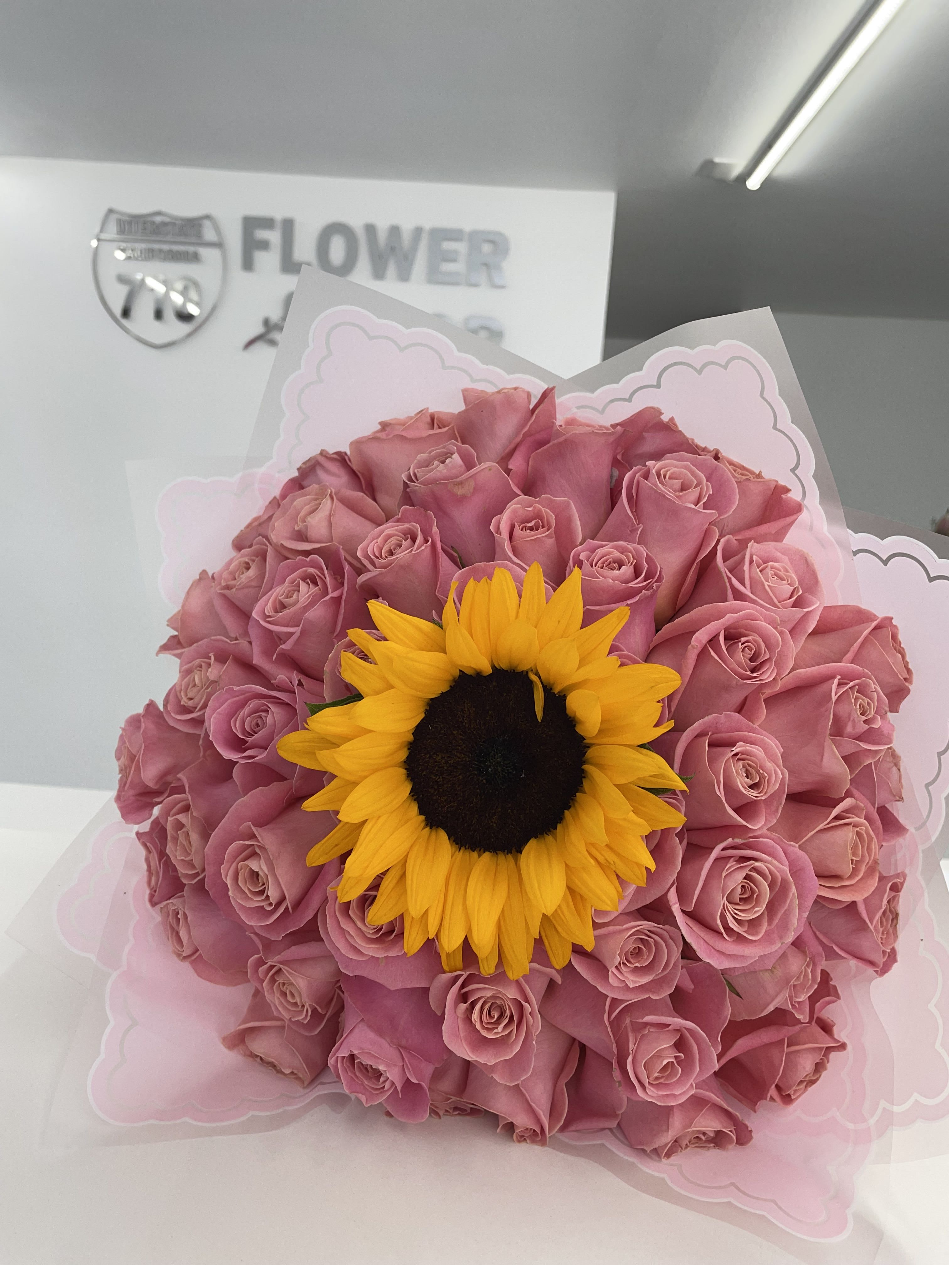 Pink Ramo Buchon With Sunflower Pink Ramo Buchon With Sunflower - Beautiful Ramo Buchon in pink of 50 roses with 1 sunflower in the center! If you'd like a specific color of paper please add to the notes what color you'd like! (Does not come in a vase, this is a wrapped bouquet. The stems will also be wrapped in paper with bow on the bottom. If paper is not available, we will pick one similar.)