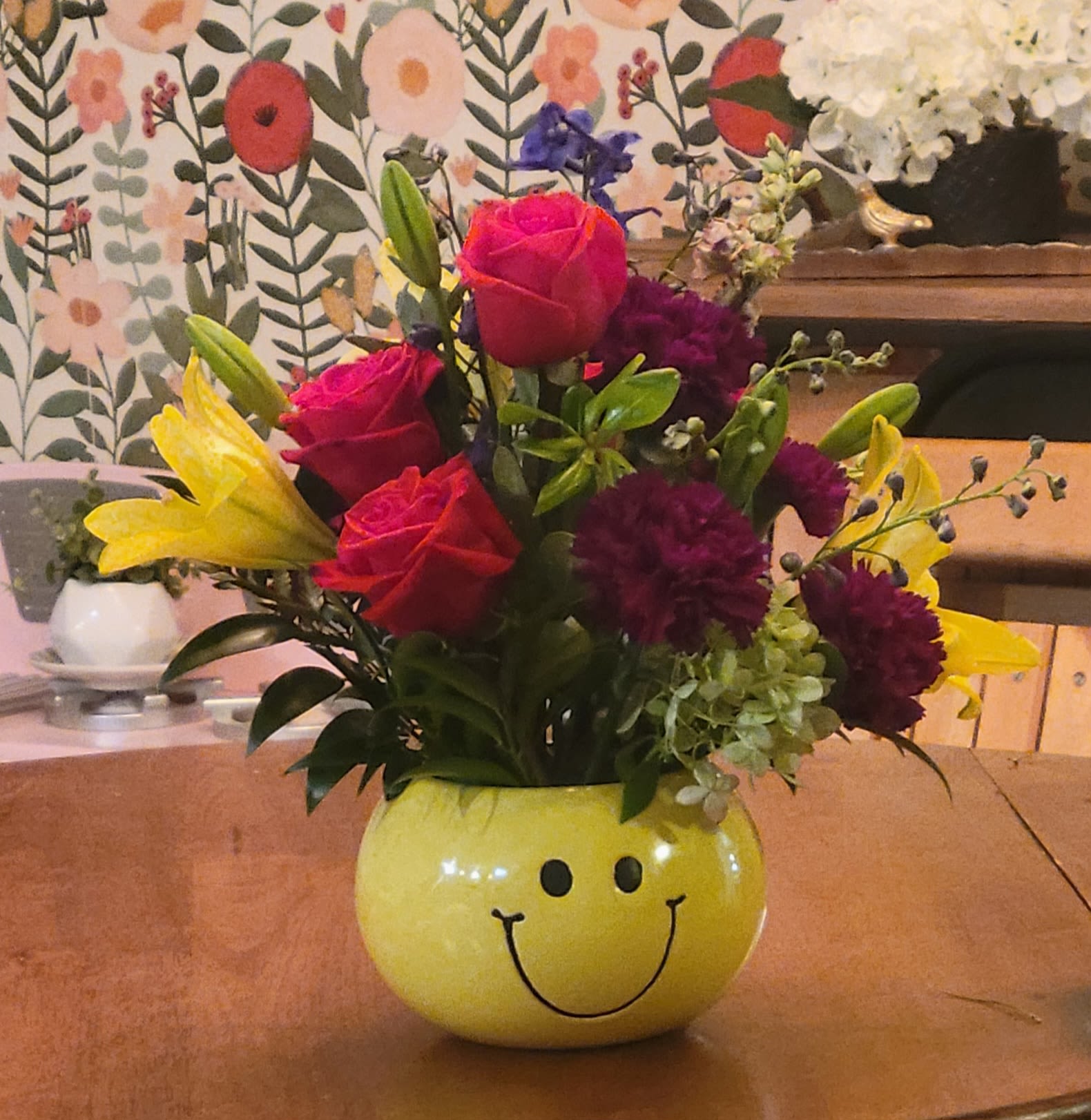 Happy by Dixie's Flowers Happy by Dixie's Flowers - “A burst of sunshine and smiles! Bright lilies, roses, and carnations in a happy-face vase—perfect for lifting spirits and brightening any day.”