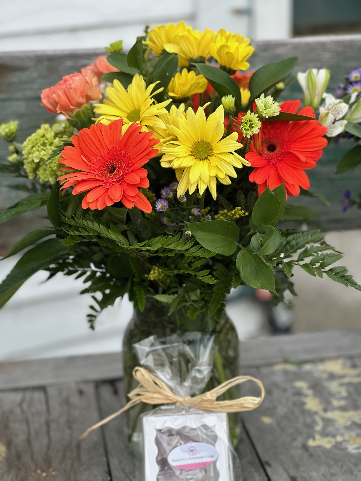 Deal of The Day-Sunshine Bqt fudge included - Deal of The Day-Sunshine Bouquet with Ralphina's Homemade fudge Orange Gerberas, yellow daisys, green hydrangea, orange carnations, white alstromeria and purple monte arranged in our popular milk jug vase 