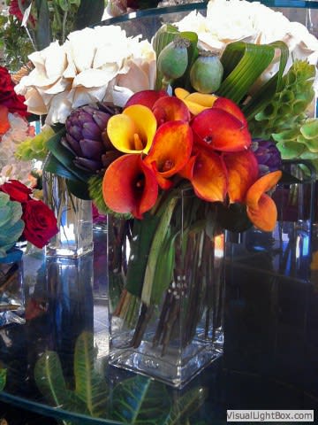 Modern Square Arrangement - Modern square arrangement with height. Large clusters of roses with mini calla lilies, opium pods, and greens. Dimensions: 18-24 in height, 12-16 in diameter.