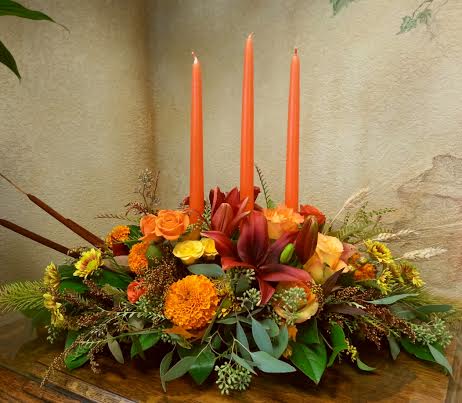 Thanksgiving Glow Thanksgiving Glow - A heart warming centerpiece with three candles, roses, lilies, and mums. This arrangement is approximately 22 inches long.
