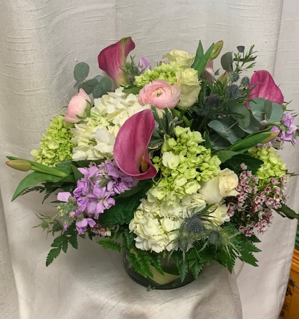 Love at first sight (DL) - This arrangement boasts a delicate fusion of white and green Hydrangea, dark pink mini Callas, white Roses, lavender Stock, blush pink Ranunculus, pink Waxflowers, Thistle, lavender Tulips, Eucalyptus, and assorted greens. Skillfully hand-crafted by our expert florists, each bloom is meticulously arranged in a 6x6&quot; glass cylinder vase to create a stunning visual masterpiece. 