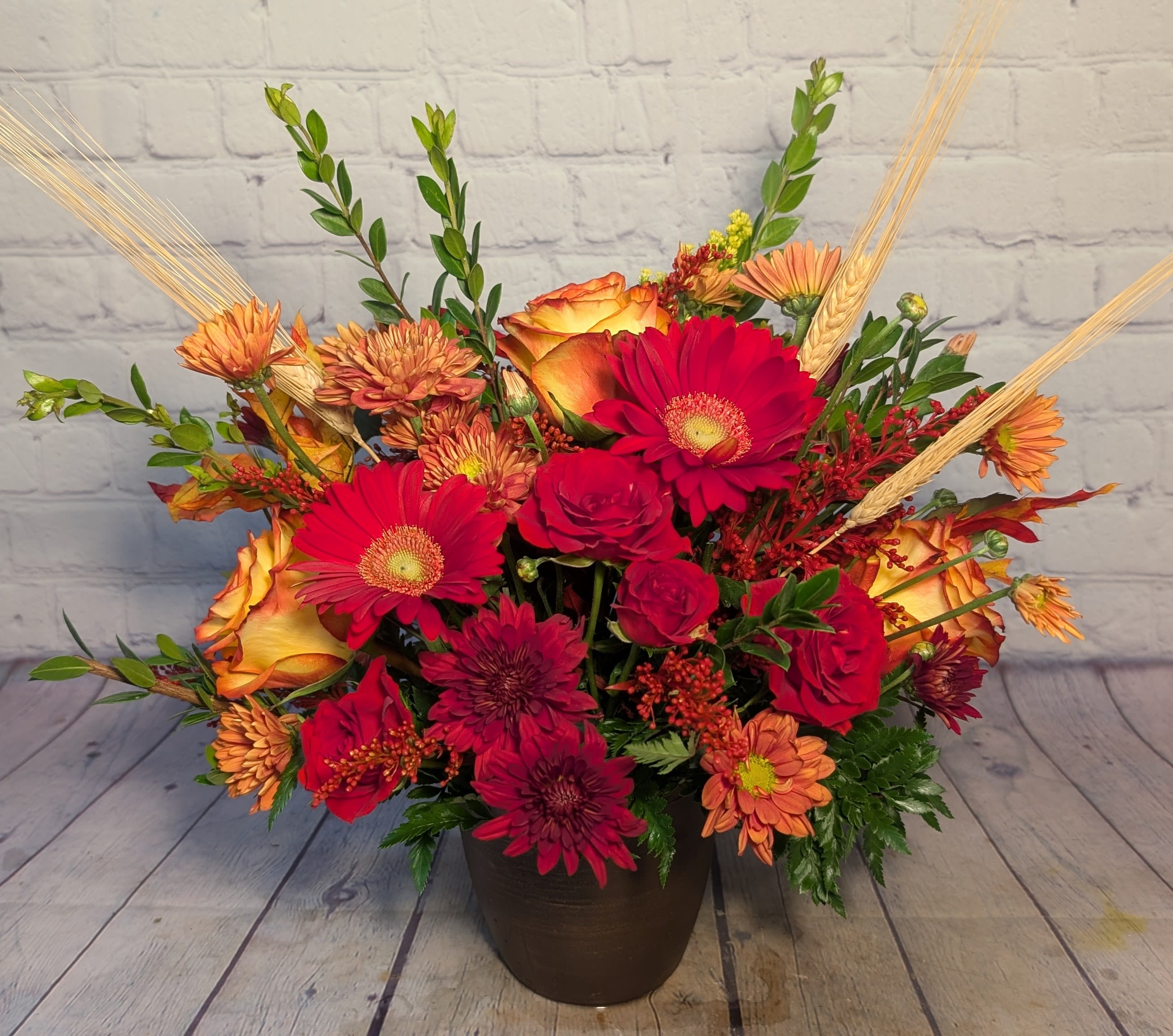 Spiced Cider - Warm and inviting, Spiced Cider captures the cozy spirit of fall in full bloom. This vibrant mix features red mini Gerber daisies, orange roses, red spray roses, orange daisies, yellow solidago, and seasonal accents of glycerin leaves and wheat. With rich tones of orange, red, and a hint of golden yellow, it’s the perfect arrangement to celebrate the beauty and warmth of the season.