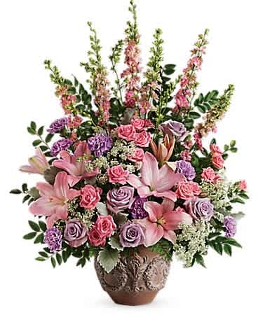 Teleflora's Soft Blush Bouquet - A touching tribute to a beloved woman, this beautiful, soft pink and lavender arrangement is presented in a large antiqued pot for an elegant touch. This soft pink arrangement features lavender roses, pink spray roses, pink asiatic lilies, lavender carnations, pink larkspur, queen anne's lace, huckleberry, dusty miller, and leatherleaf fern. Delivered in a Classical Garlands pot.