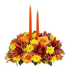 Harvest Candlelight Elegance Harvest Candlelight Elegance - Warm your table with the rich beauty of fall! This stunning centerpiece features vibrant orange lilies, golden chrysanthemums, and lush roses accented with berries and greenery. Two elegant taper candles rise above the blooms, adding a cozy glow perfect for Thanksgiving gatherings or any autumn celebration.