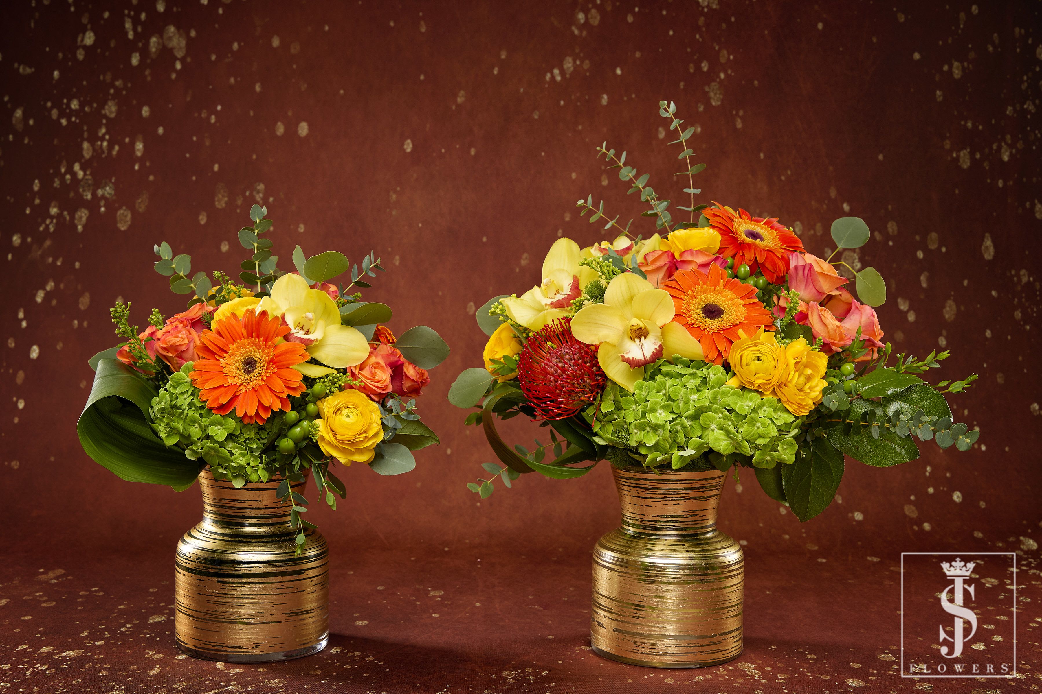 Golden Sunset Blooms - Brighten any room with the vibrant warmth of the Golden Sunset Blooms. This stunning arrangement features a rich blend of orange Gerbera daisies, yellow orchids, radiant roses, and lush green hydrangeas, nestled among eucalyptus and other greenery. Presented in an elegant gold-rimmed vase, this floral display is perfect for adding a luxurious touch to any occasion, be it a celebration or a simple gesture of appreciation.