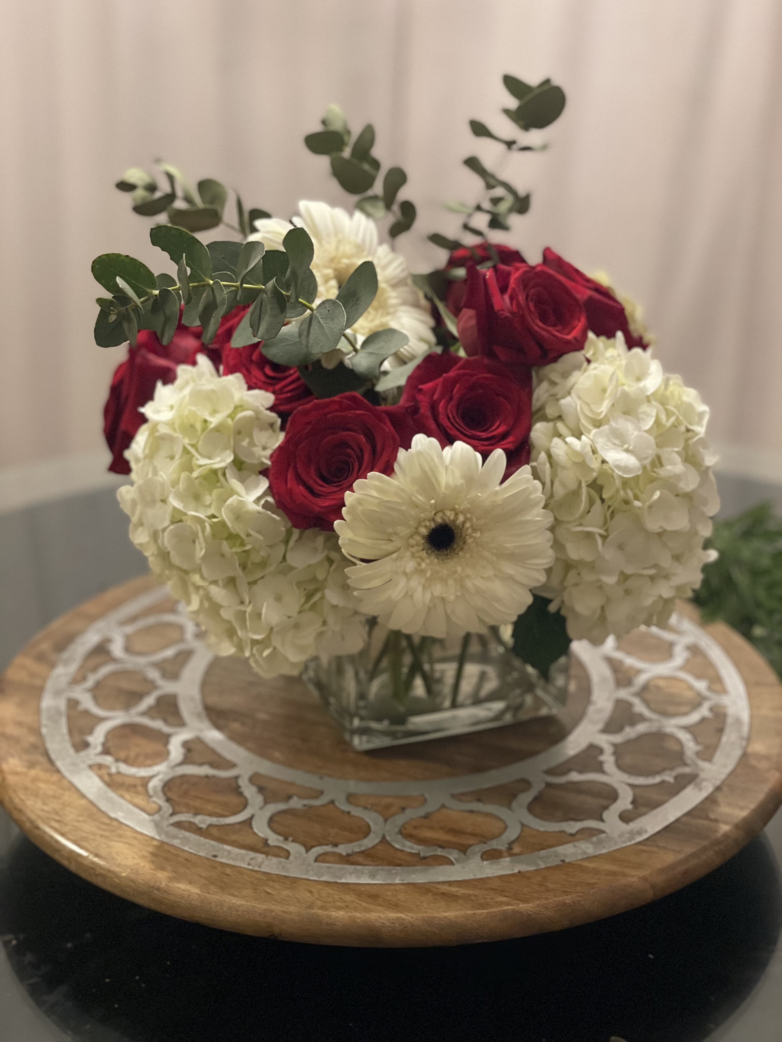 Classic Elegance - Timeless and sophisticated, Classic Elegance captures the essence of refined beauty. This stunning arrangement features lush white hydrangeas, radiant red roses, and crisp white gerbera daisies, accented with fresh eucalyptus in a sleek glass cube vase. Perfect for romantic occasions, celebrations, or simply elevating any space, this bouquet exudes charm and grace in every petal.
