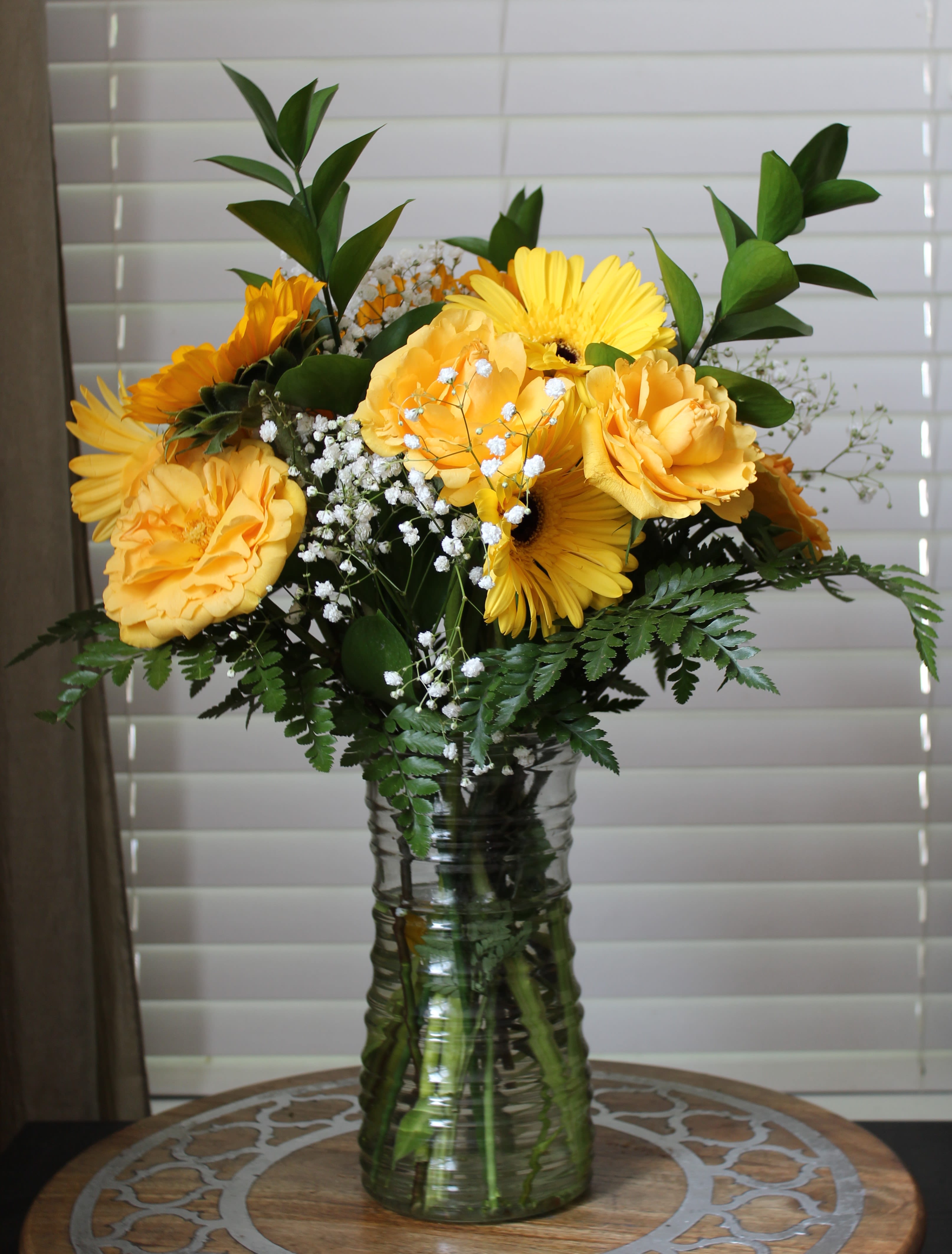 Sunshine Bouquet - Radiate happiness and warmth with our Sunshine Bouquet, a vibrant mix of yellow roses, cheerful gerbera daisies, and golden sunflowers artfully arranged in a clear glass vase. This sunny combination captures the essence of joy, optimism, and friendship — perfect for brightening someone’s day.  Each bloom is carefully selected for its radiant color and fresh, long-lasting beauty. The lush greenery and textured accents bring a natural balance to the bold yellow tones, creating a design that feels as uplifting as a summer morning.  Includes: Bright yellow roses Sunny yellow gerbera daisies Fresh, golden sunflowers Seasonal greenery and filler Clear glass vase  Ideal for birthdays, congratulations, or just because — the Sunshine Bouquet delivers smiles and light wherever it goes.