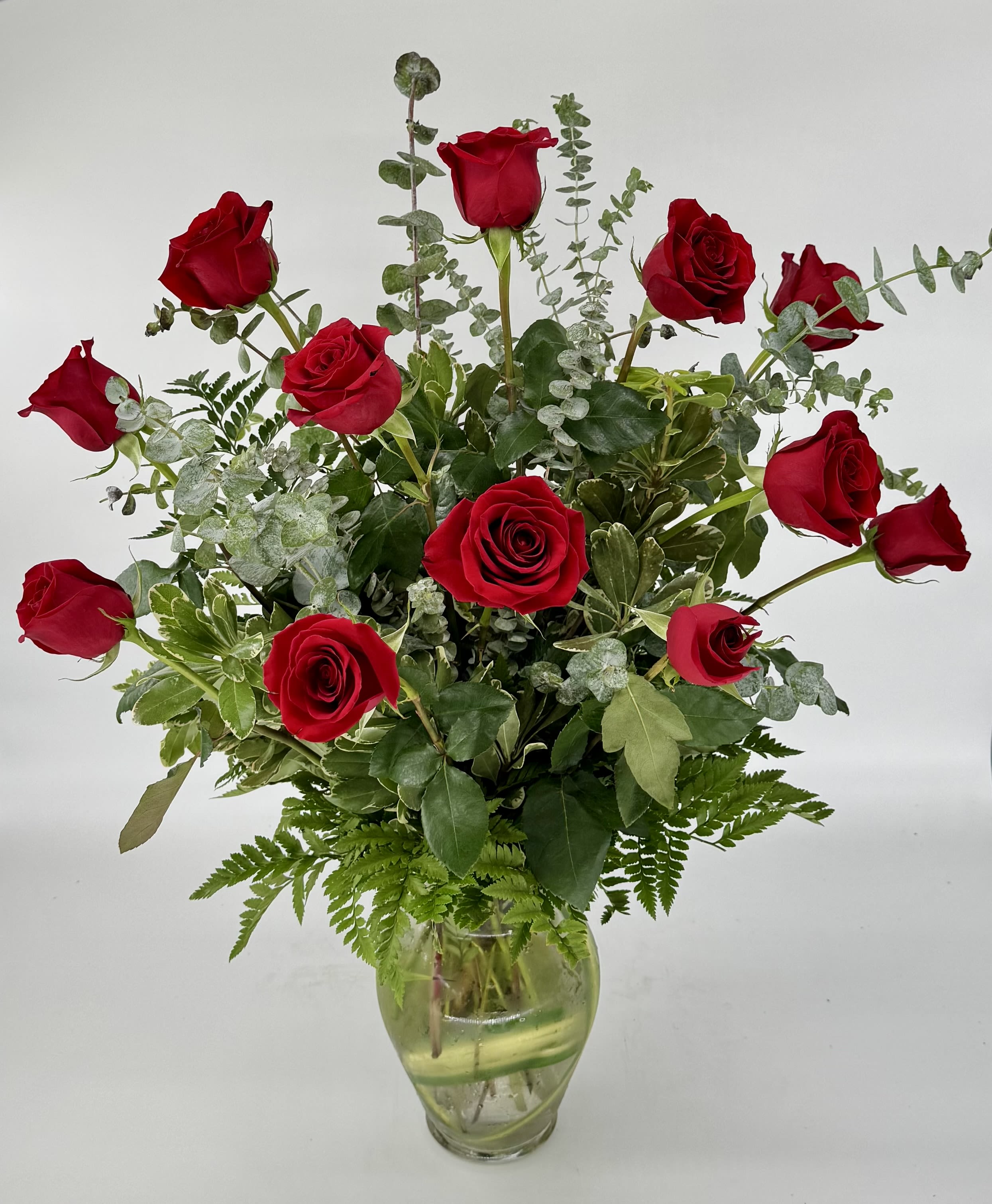 Red Roses (DB) - Immerse your loved one in timeless elegance with a dozen long-stemmed red roses, artfully arranged in a clear glass vase and thoughtfully accented with fresh eucalyptus and lush greens—because your moments deserve perfection.