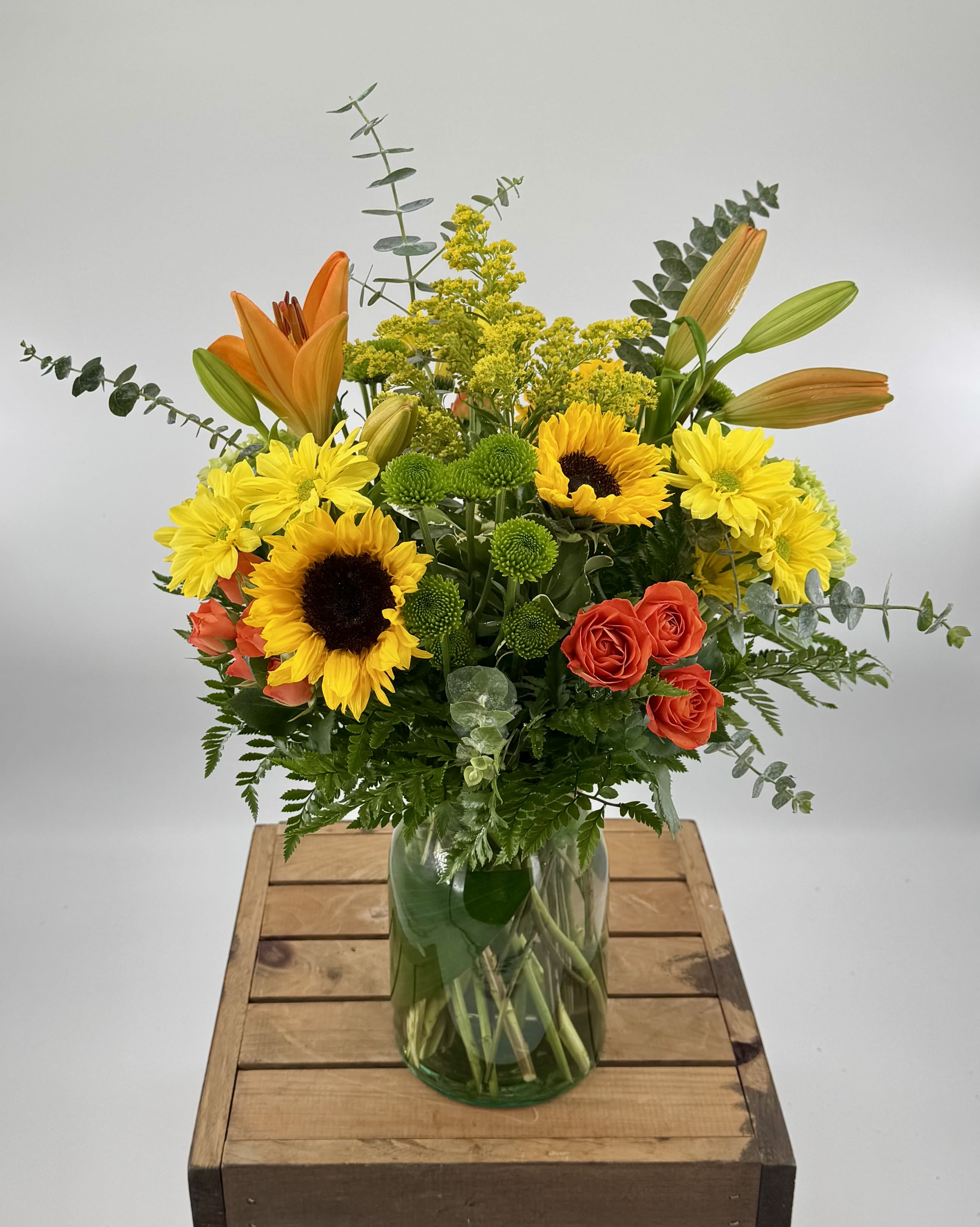 Thankful for You (DB) - Capture the spirit of autumn with this vibrant floral arrangement featuring orange lilies, delicate spray roses, radiant sunflowers, and fresh eucalyptus—perfectly blending warm hues and textures to bring cozy, seasonal elegance to any setting.