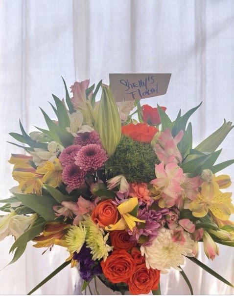 Radiant Garden By Shelly -  A lively burst of color and elegance, this arrangement is designed to impress. Full of lush textures and vibrant tones, it captures the joy of a flourishing garden in full bloom. Carefully hand-crafted and arranged in a stylish vase, it makes a stunning centerpiece for any occasion.  Go from thoughtful to unforgettable