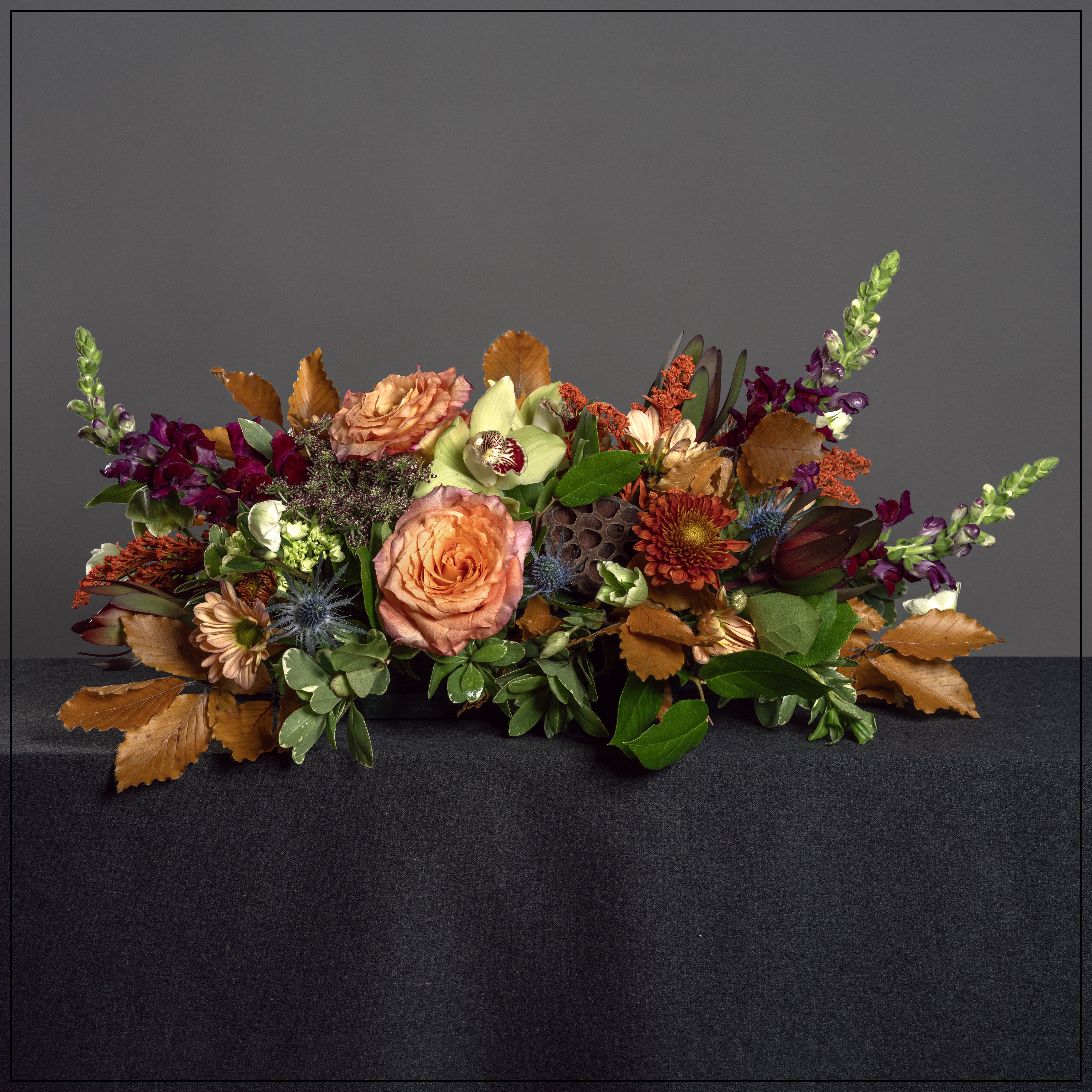 Breaking Bread Breaking Bread - For all of those autumn gatherings, a centerpiece of roses, mums, hydrangea, snapdragons, eryngium and hellebore in a lie flat tray. Dimensions: 12" H x 22" L x 12" W