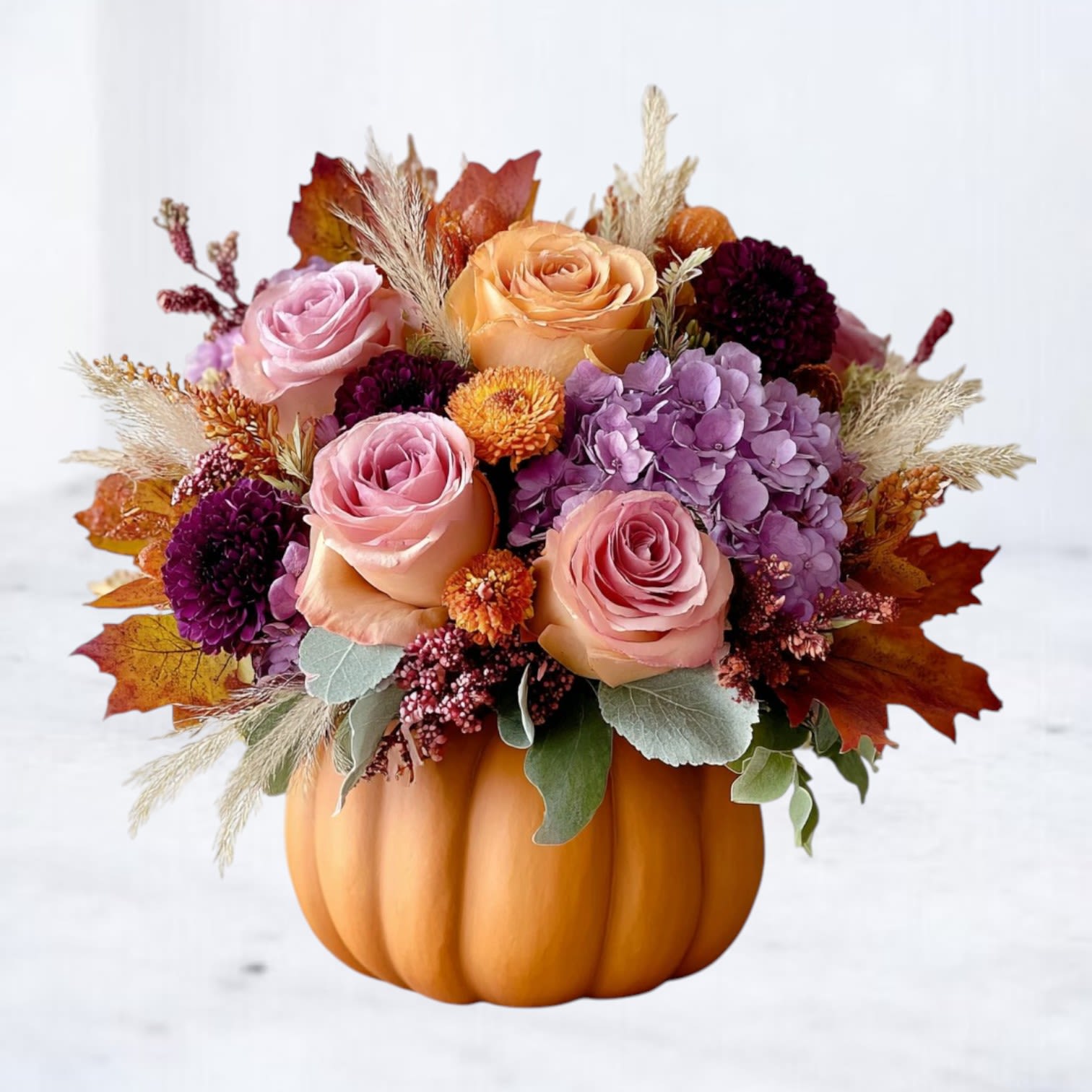 Copperling Copperling - A study in warmth and texture, Copperling embodies the quiet poetry of autumn. Nestled in a natural pumpkin vessel, this luxe composition blends peach and mauve roses, plum chrysanthemums, and violet hydrangea with dried accents and autumn foliage. The effect is both painterly and refined — a modern ode to fall’s fleeting beauty. Designed to elevate any table, entryway, or gathering, Copperling captures the delicate balance between soft romance and seasonal richness. It’s the perfect statement for harvest dinners, birthday celebrations, or simply savoring the season’s golden glow.
