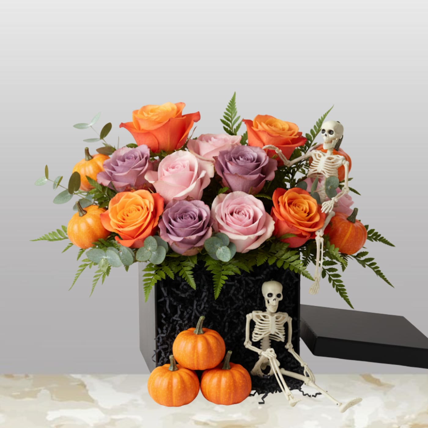 The Halloween Twilight Rose Box The Halloween Twilight Rose Box - Give a thrilling gift with our Halloween Twilight Rose Box! This arrangement perfectly captures the spirit of the season, blending elegant roses with a fun, spooky twist. It’s the ultimate statement piece for Halloween parties, a unique fall birthday gift, or a charmingly macabre surprise for someone special. What's Inside This Hauntingly Chic Box? This unique set transforms a beautiful dozen roses into an unforgettable Halloween centerpiece. 12 Vibrant Roses: A stunning mix of sunset orange, mystic lavender, and soft pink roses that evoke the magic of an autumn sunset. The Black Box: The flowers are stylishly presented in a chic black square box, giving the arrangement a modern, dramatic look. Spooky Accents: Adding to the fun are three playful mini-pumpkins and a little skeleton figure resting artfully among the blooms and leaves. Perfect for Your Ghoul-Friends This arrangement is much more than a bouquet—it's instant Halloween flair! Hostess Gift: The perfect way to thank your Halloween party host. Unique Decor: A sophisticated yet spooky centerpiece for any fall table. A Spooky Surprise: Send a smile to the person who loves all things macabre and marvelous. Order the Halloween Twilight Rose Box today for a uniquely beautiful way to celebrate the season!