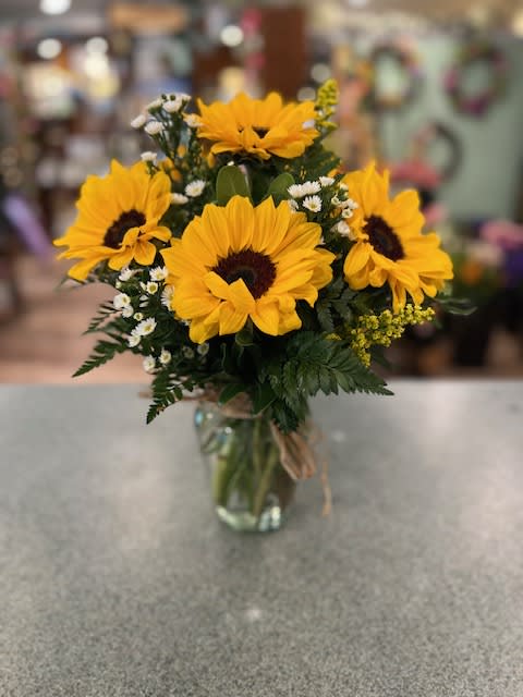 Country Sunflowers (CS) - *** VASE SYLE MAY DIFFER FROM PICTURED*** Everyone likes sunflowers! One of our most popular vase, Fresh sunflowers and choice accent flowers designed in a clear vase tied off with raffia.