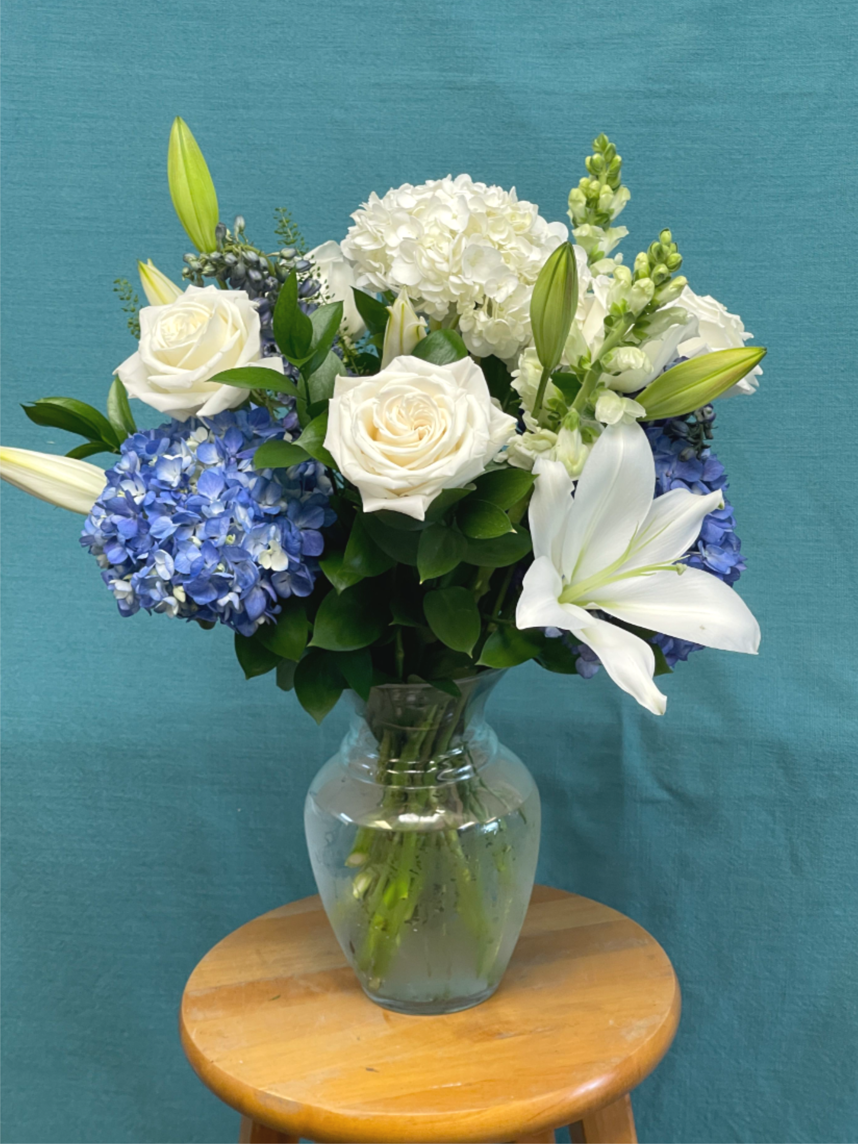 Breezy by the Ocean Breezy by the Ocean - Elegant and serene, this arrangement features white lilies, roses, and hydrangeas in soft shades of blue and cream. Designed in a clear glass vase, it’s perfect for any occasion — bringing freshness, grace, and peaceful beauty to any space. in 10" glass vase