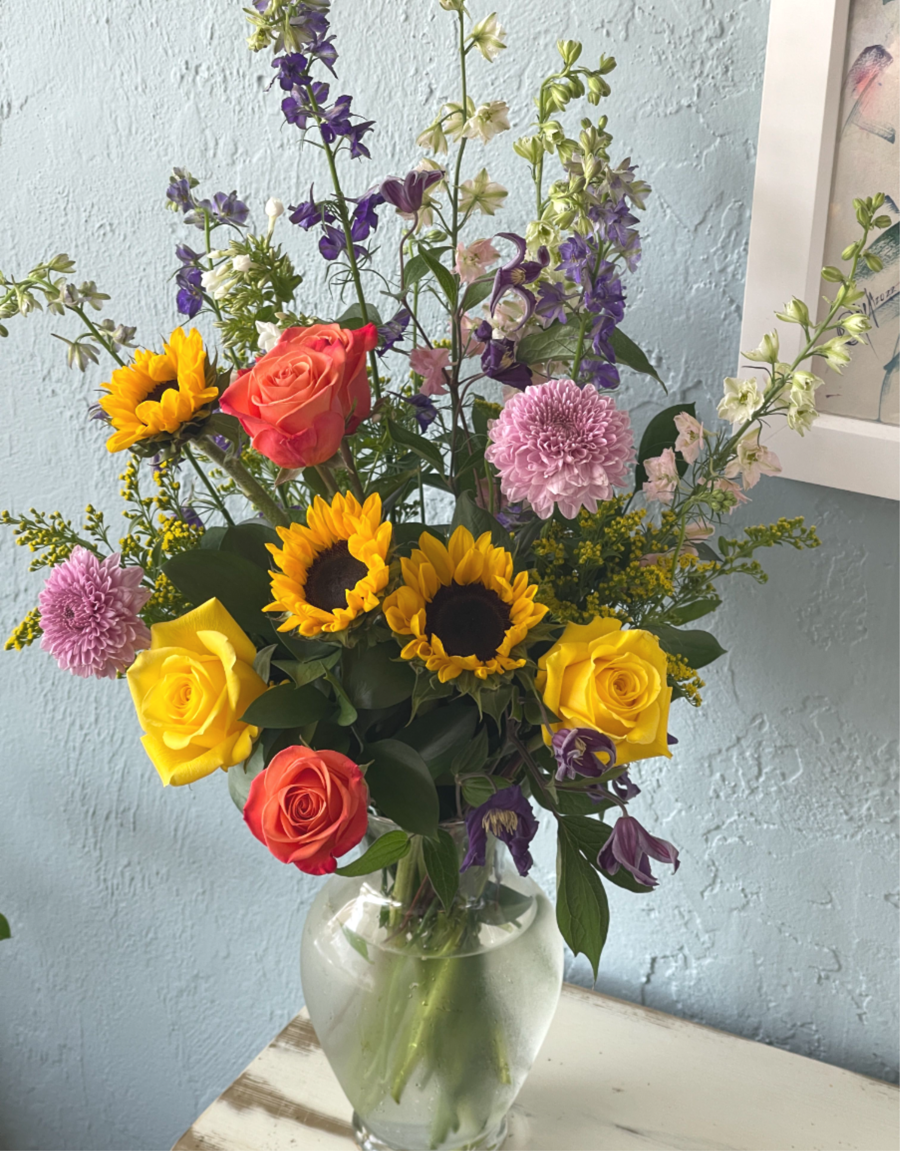 Diana Diana - Show your appreciation with this sweet, fun bouquet. This arrangement contains white sunflowers, orange and yellow roses, and delphinium . Perfect gift for Mother's Day, Birthday, or Just Because. APPROXIMATE DIMENSIONS: 10" H X 16" W
