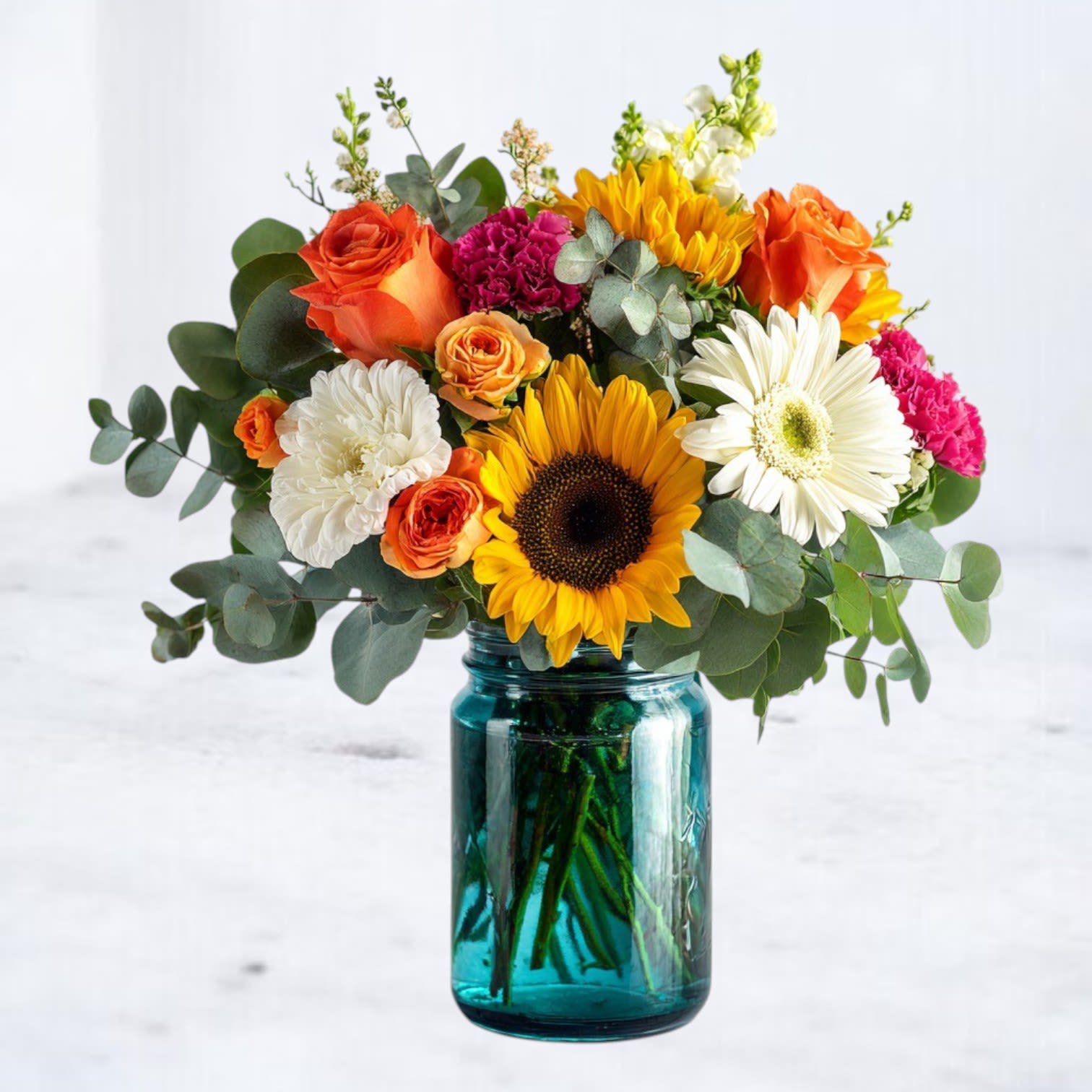 Daybright Bouquet Daybright Bouquet - Bring sunshine indoors with our Daybright Bouquet, a joyful mix of sunflowers, roses, gerbera daisies, carnations, and snapdragons, all arranged in a charming teal mason jar vase. This design combines the rustic warmth of farm-fresh blooms with a modern, cheerful twist — perfect for birthdays, get well wishes, or simply to brighten someone’s day. Crafted by our designers with bold pops of yellow, orange, pink, and white, this bouquet radiates energy and happiness. The playful mason jar container adds a welcoming touch, making it easy to enjoy at home, in the office, or as a thoughtful surprise for someone special. Order the Daybright Bouquet with same-day flower delivery in Houston, Magnolia, The Woodlands, Spring, Tomball, Cypress, and surrounding areas. Whether you’re sending birthday flowers, a cheerful pick-me-up, or just because, this sunflower arrangement is sure to deliver smiles.