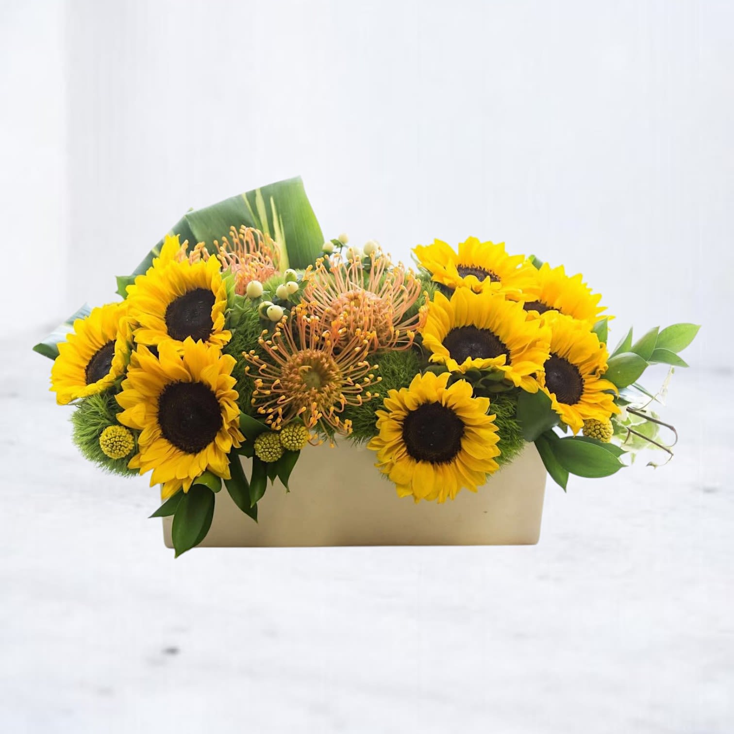 Atomic Bloom Atomic Bloom - Bursting with bold energy and striking texture, Atomic Bloom is a modern sunflower arrangement that turns heads and sparks conversation. Golden sunflowers, vibrant pincushion protea, and playful craspedia balls are artfully arranged with moss and fresh greenery in a sleek, rectangular vase—perfect for someone with a love for contemporary design and joyful florals. Whether you're celebrating a birthday, sending sunshine to a loved one, or decorating a corporate space, this radiant display delivers high impact with style. Handcrafted and available for same-day delivery across Houston, The Woodlands, Conroe, Spring, and Magnolia, Atomic Bloom is a standout for any occasion.